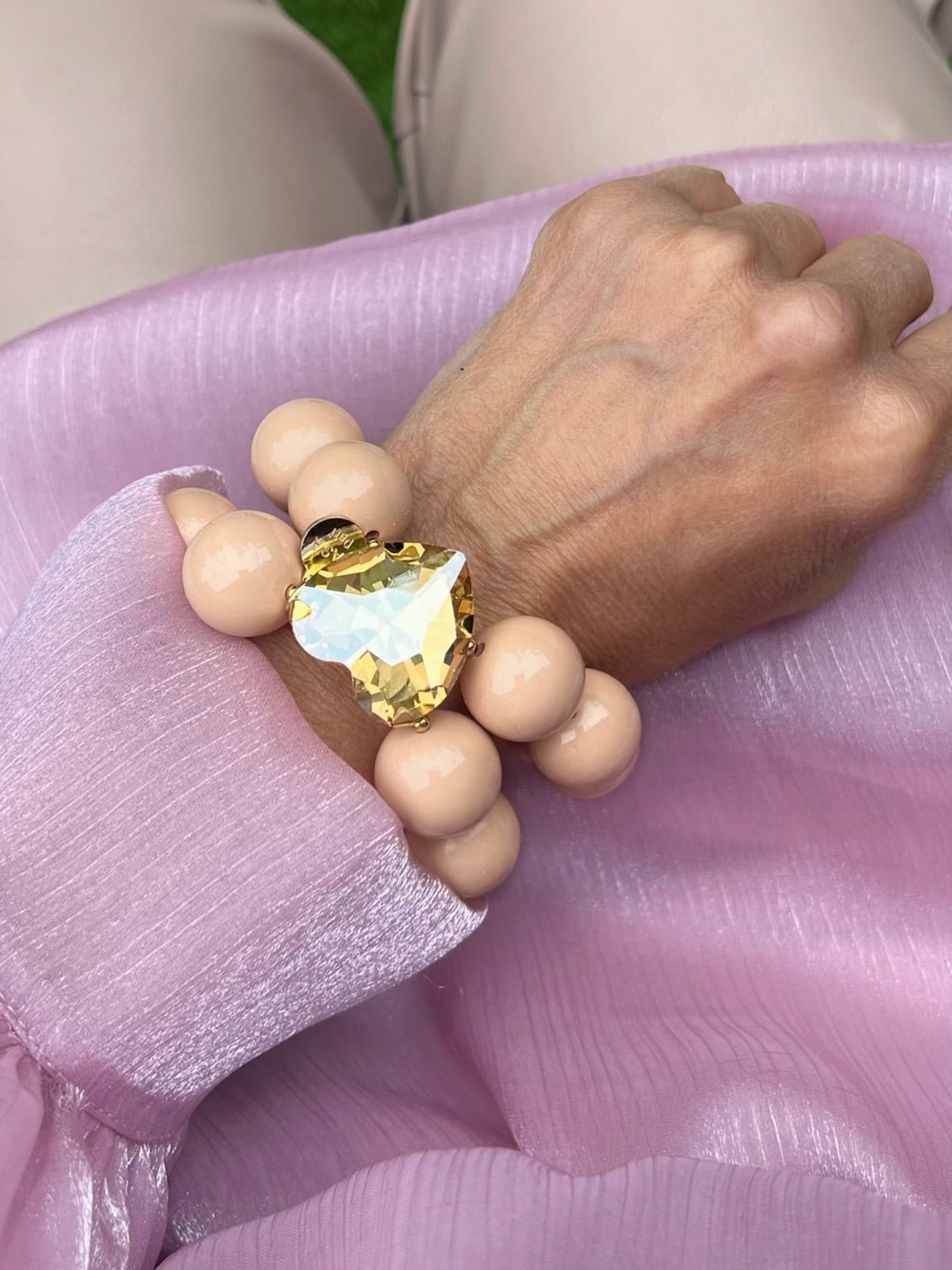 Armband in Hellbeige mit großem Herzschmuckstein. Am Handgelenk auf rosa Stoff fotografiert.