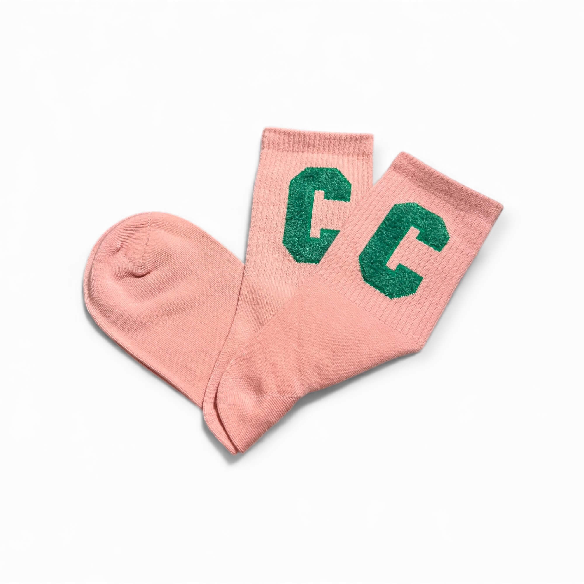 Rosa kurze Socken aus weichem Strick, flach liegend fotografiert, mit zwei grünem C-Buchstaben auf dem Schaft. Die Socken liegen leicht überkreuzt auf weißem Hintergrund.
