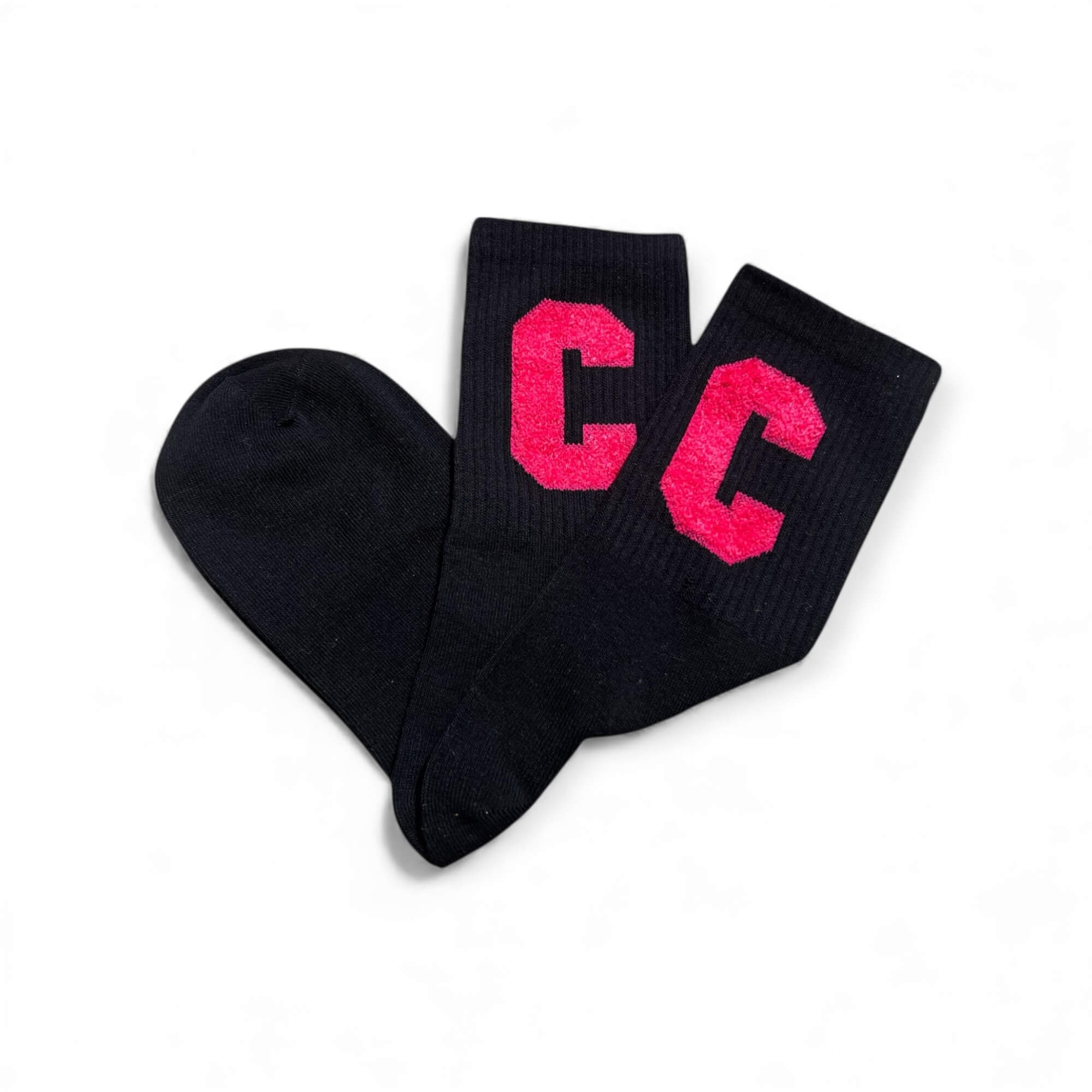 Schwarze kurze Socken aus weichem Strick, flach liegend fotografiert, mit zwei pinken „C“-Buchstaben auf dem Schaft. Die Socken liegen leicht überkreuzt auf weißem Hintergrund.