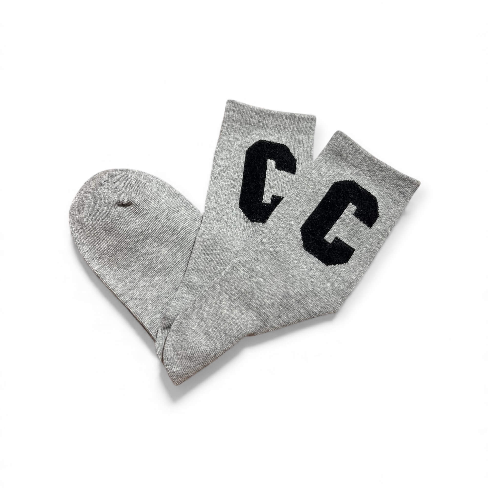 Graue kurze Socken aus weichem Strick, flach liegend fotografiert, mit zwei schwarzen „C“-Buchstaben auf dem Schaft. Die Socken liegen leicht überkreuzt auf weißem Hintergrund.