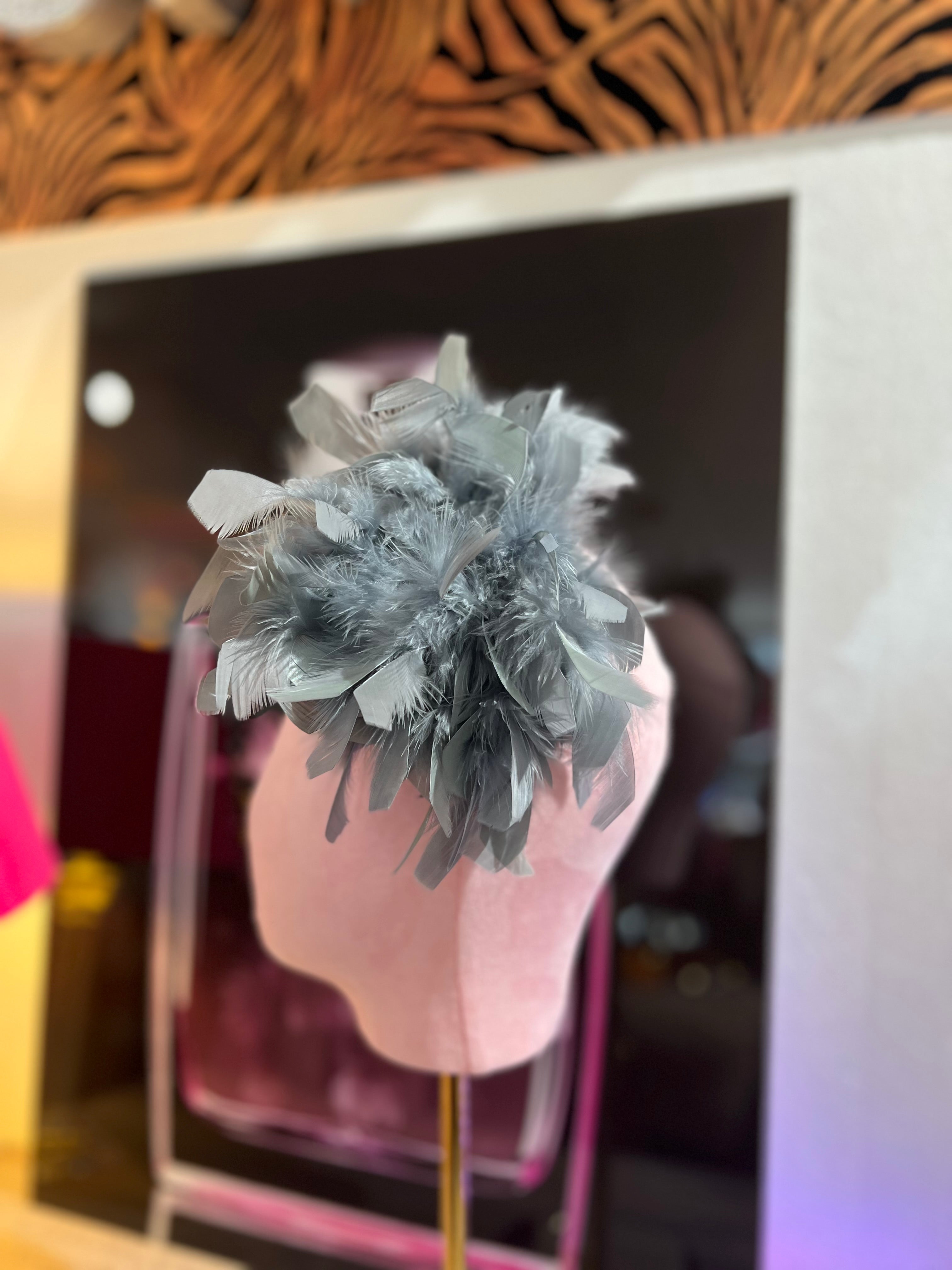 Leuchtende graue Federbrosche, kunstvoll drapiert, präsentiert auf einem rosa Samt Kopf vor einer stilvollen Kulisse.