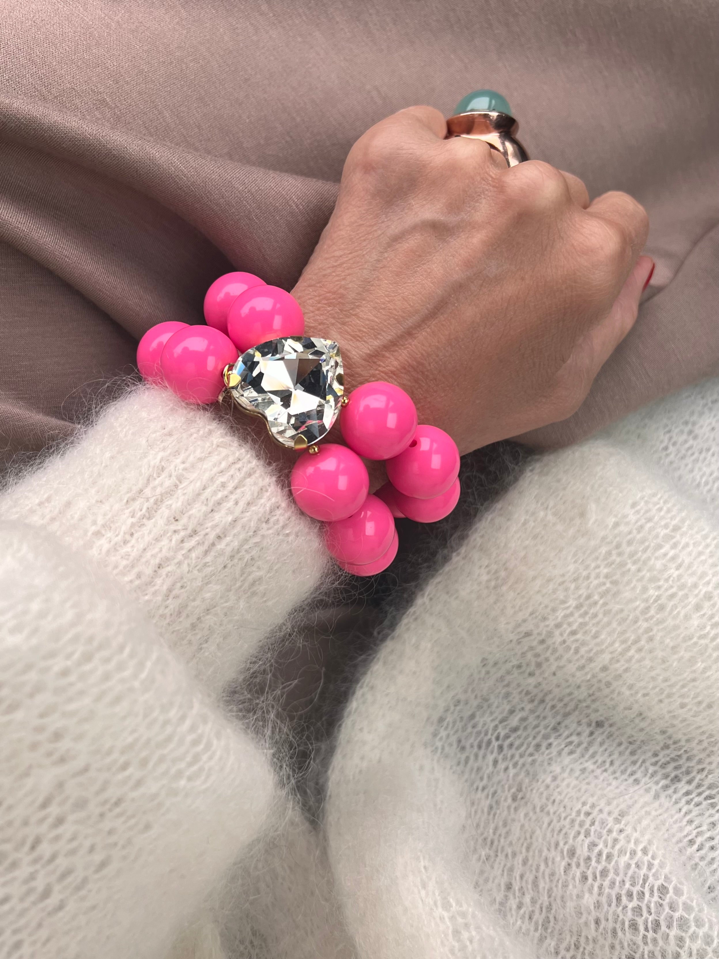 Armband in Pink mit großem Herzschmuckstein, und großem Ring. Am Handgelenk auf beigem Stoff fotografiert.