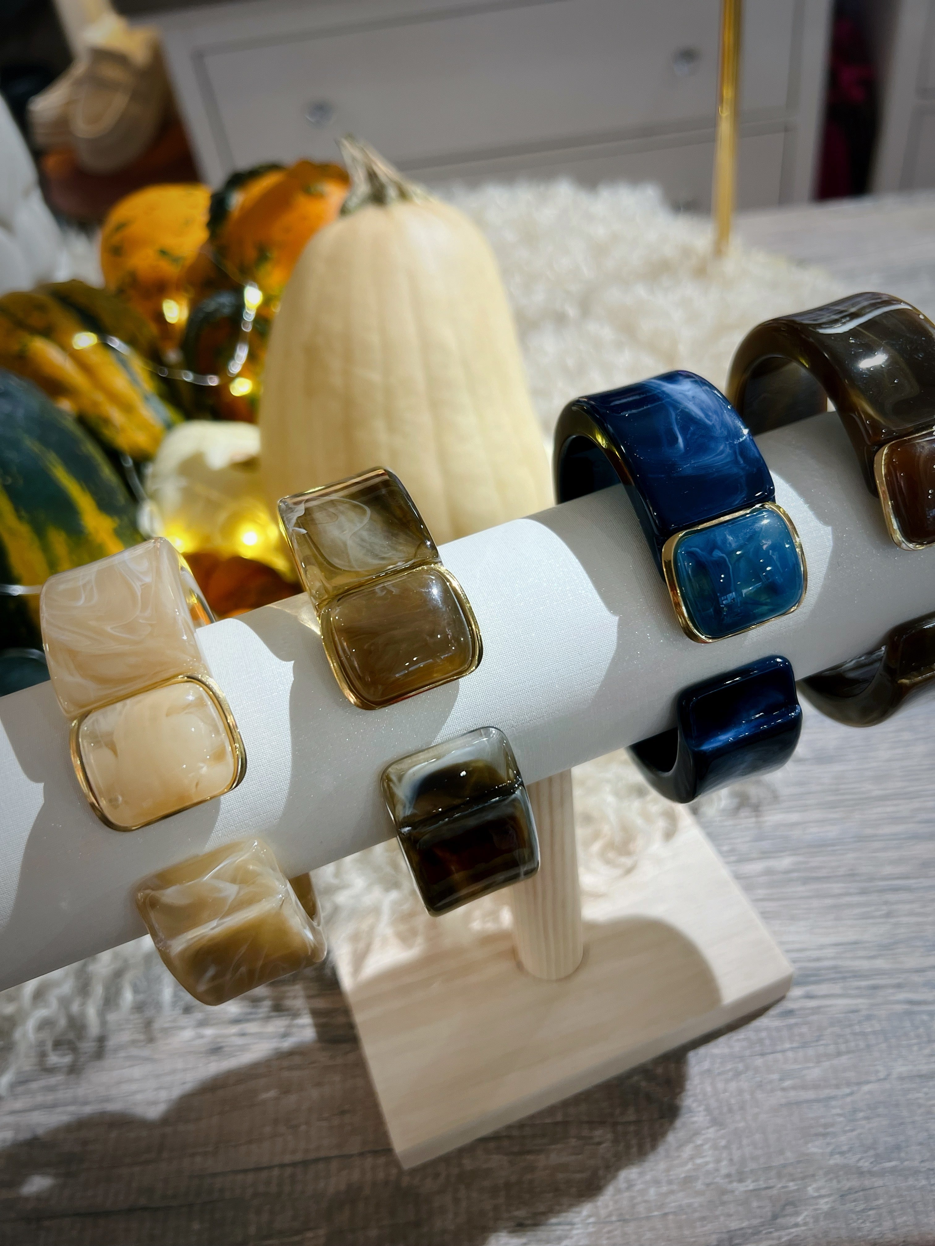 Vier Klapp Armreifen aus marmorierten Kunstharz auf einem weißen Schmuckständer. Beige, Braun und Dunkelblau, und Dunkelbraun jeweils mit goldfarbenen Details und Schmuckstein.