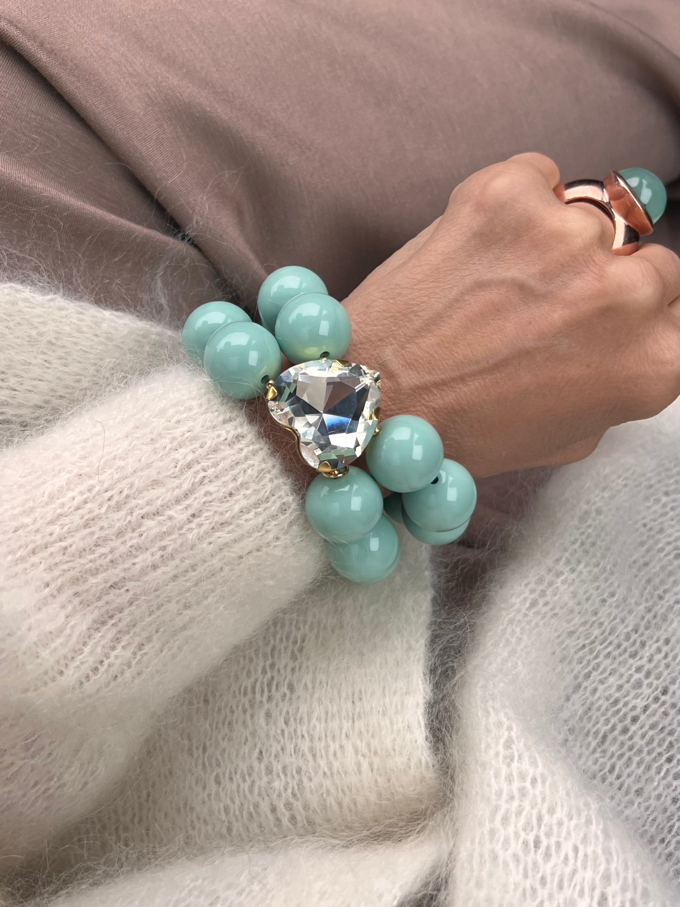 Armband in Aquafarben mit großem Herzschmuckstein, und großem Türkis Ring. Am Handgelenk auf beigem Stoff fotografiert.