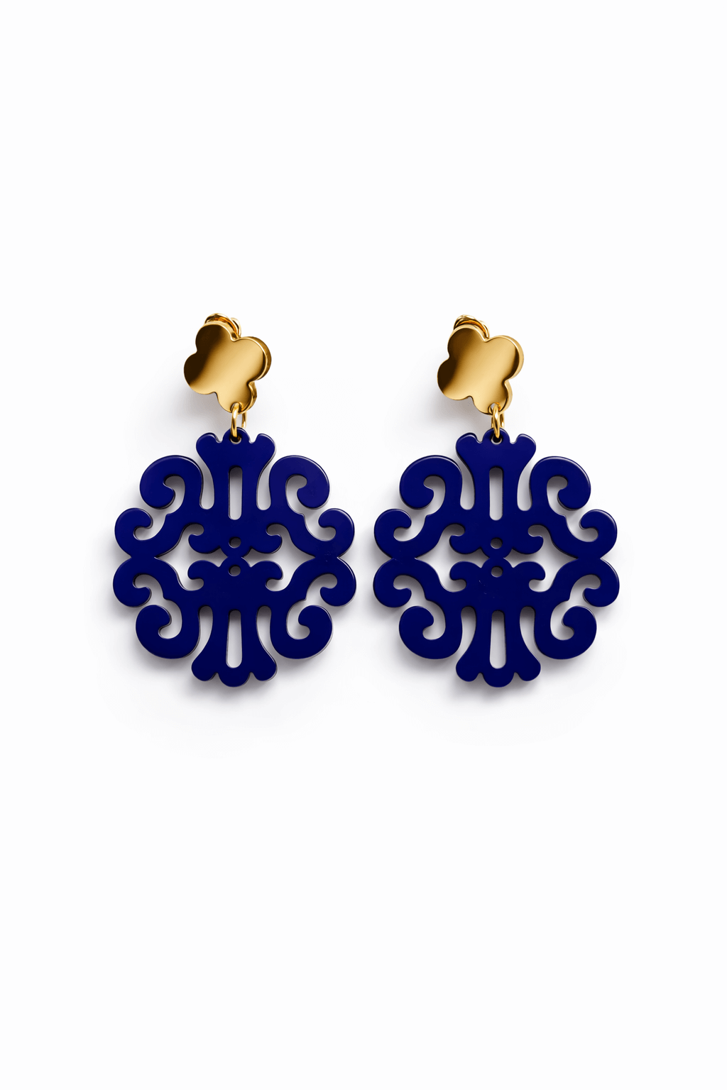 Paar hängende Ohrringe mit goldfarbenem Kleeblatt-Stecker und dunkelblauen ornamental durchbrochenem Anhänger vor weißem Hintergrund.