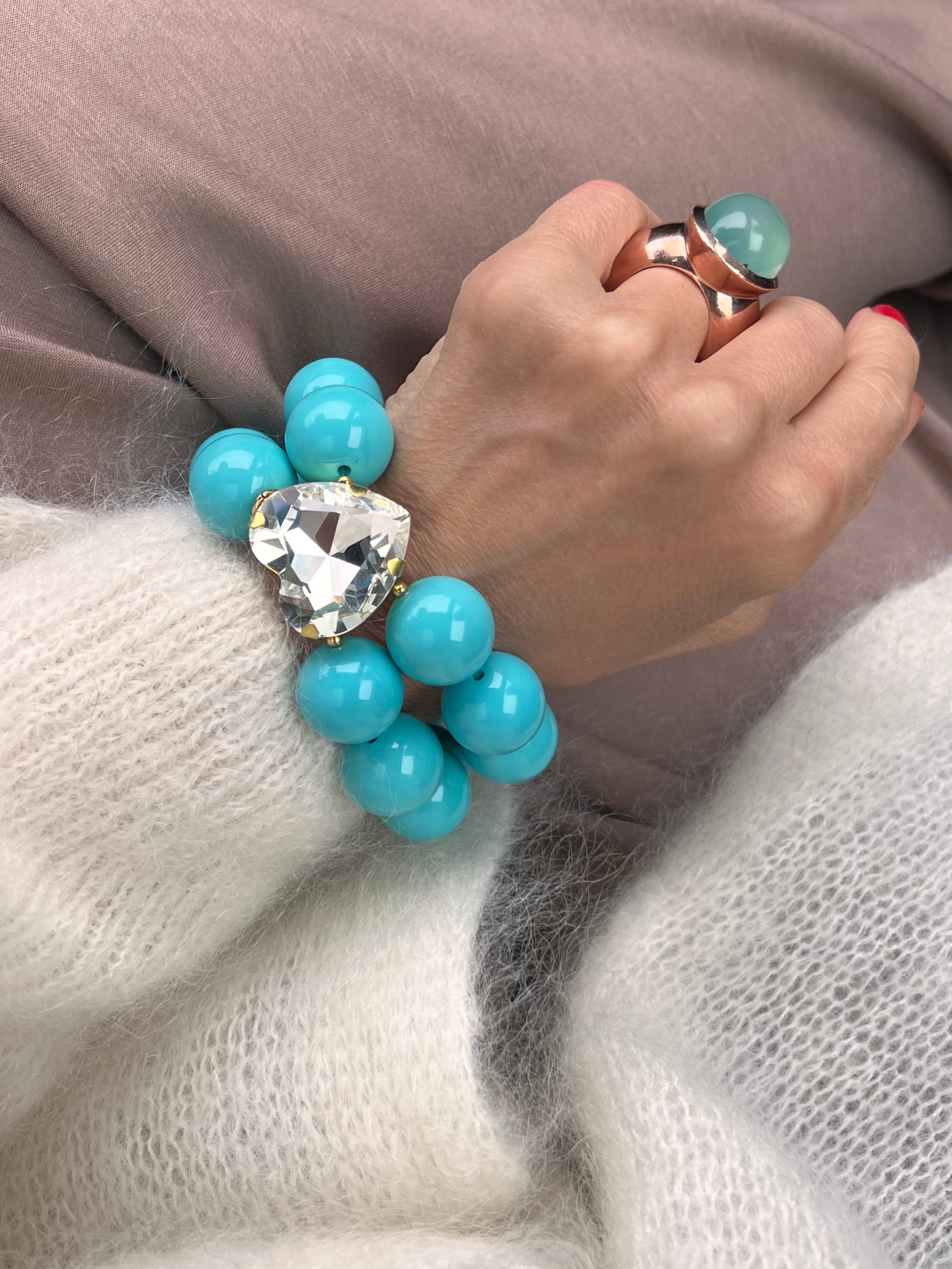 Armband in Türkis mit großem Herzschmuckstein, und großem Ring. Am Handgelenk auf beigem Stoff fotografiert.