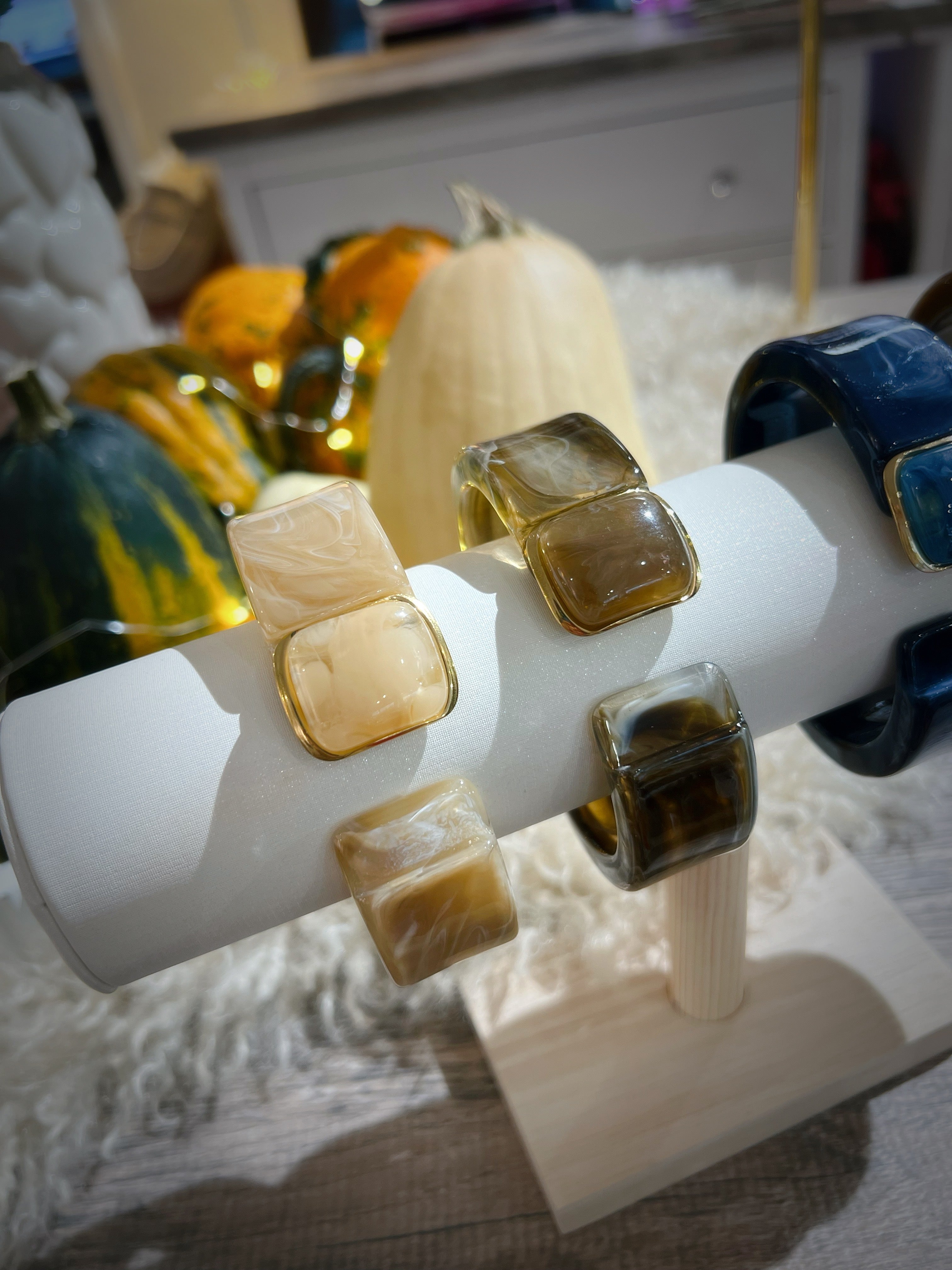 Drei Klapp Armreifen aus marmorierten Kunstharz auf einem weißen Schmuckständer. Beige, Braun und Dunkelblau, jeweils mit goldfarbenen Details und Schmuckstein.