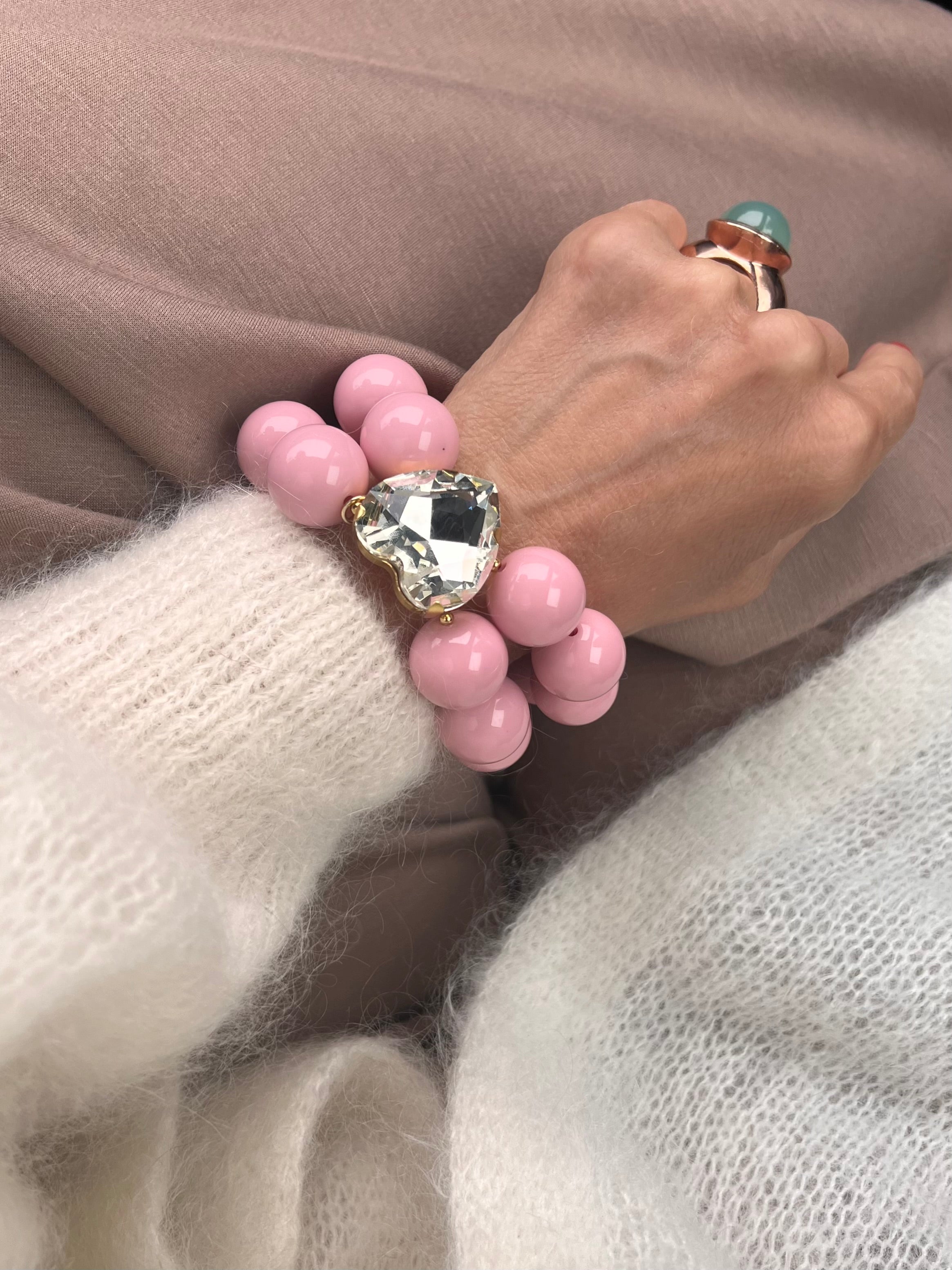 Armband in Rosa mit großem Herzschmuckstein, und großem Ring. Am Handgelenk auf beigem Stoff fotografiert.