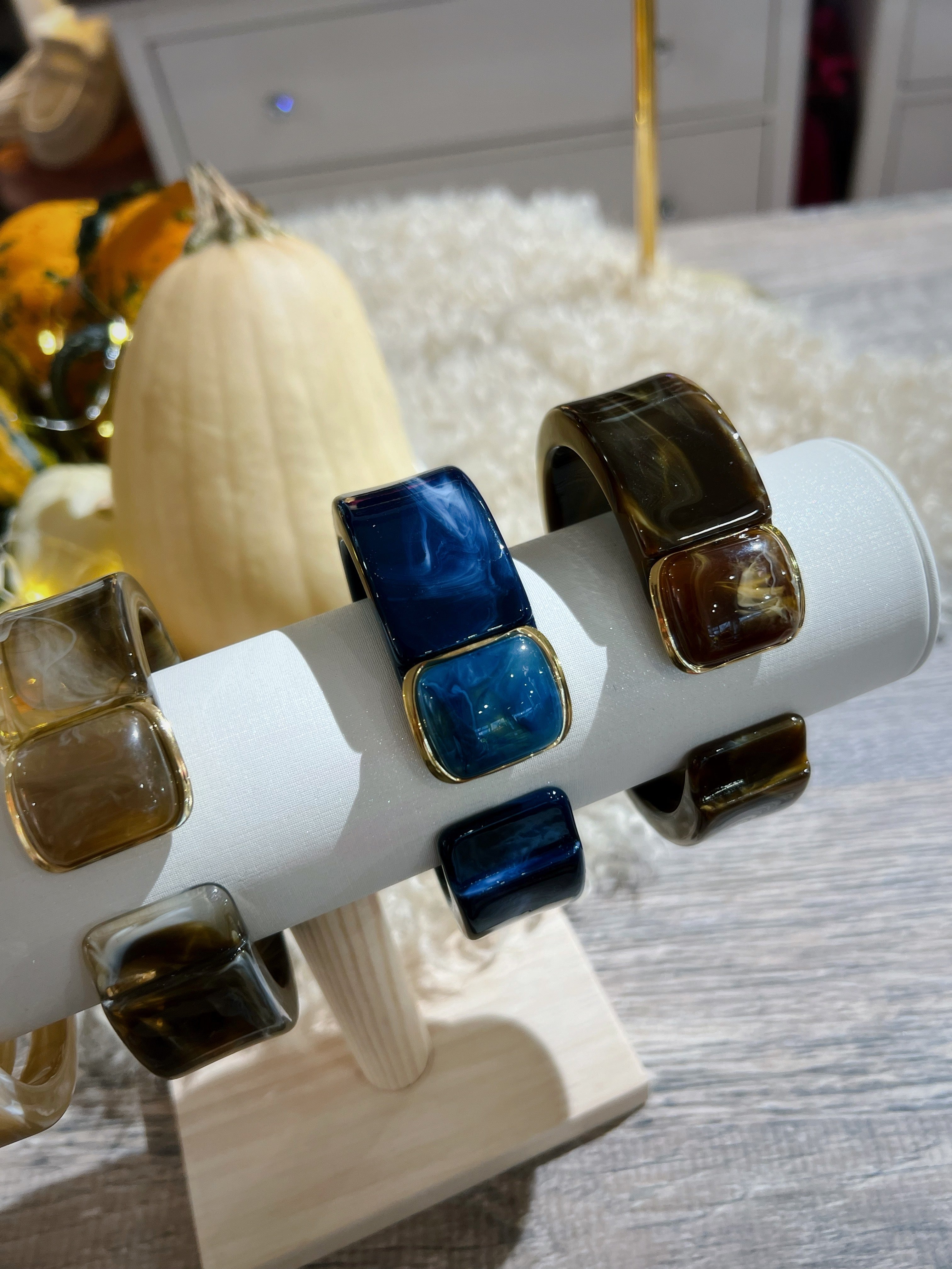 Drei Klapp Armreifen aus marmorierten Kunstharz auf einem weißen Schmuckständer. Beige, Blau und Dunkelbraun, jeweils mit goldfarbenen Details und Schmuckstein.