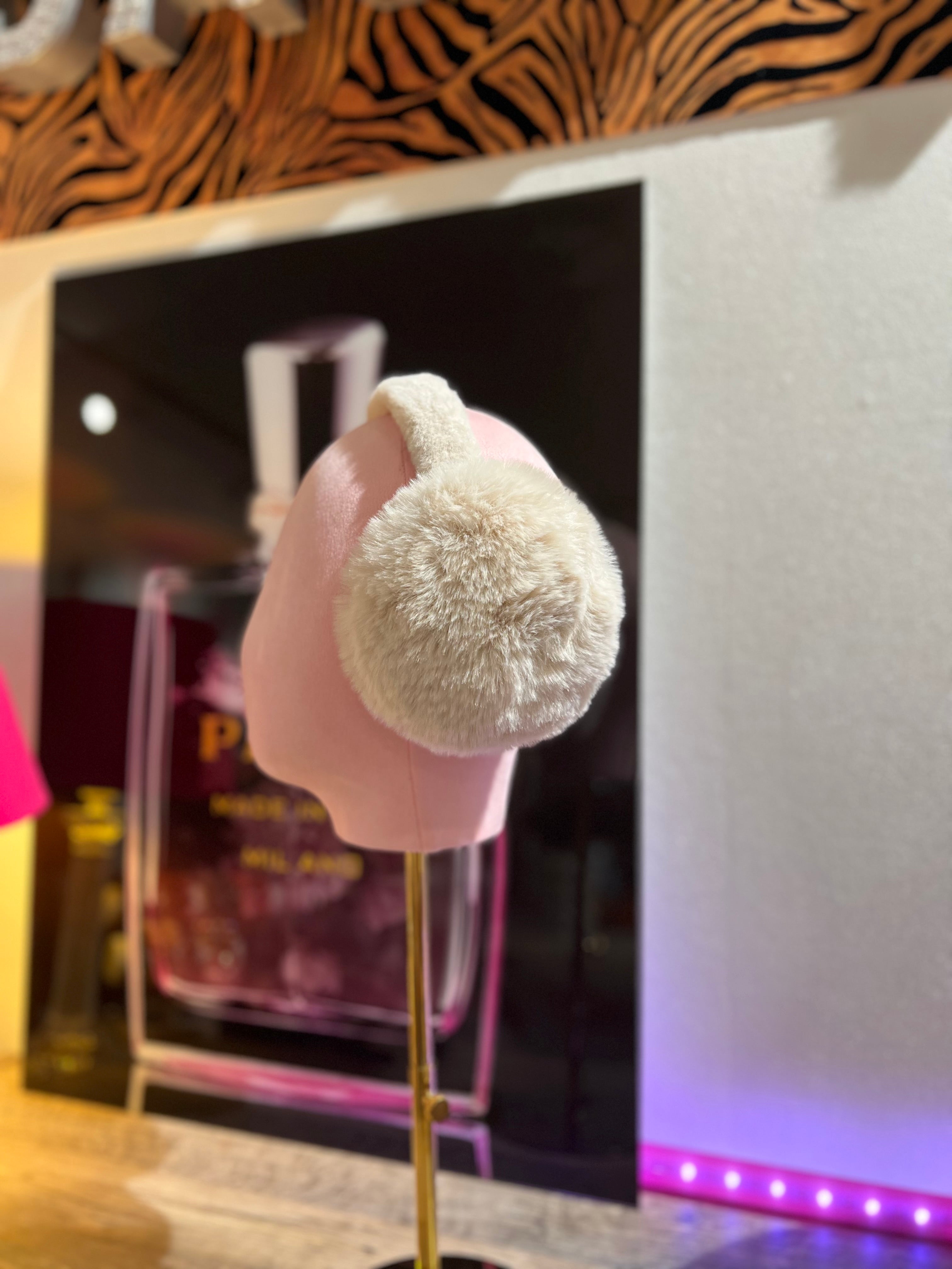Ceme, flauschige Ohrwärmer auf rosafarbene Präsentation Büste, im Hintergrund unscharf ein Parfumflakon und warme Beleuchtung.