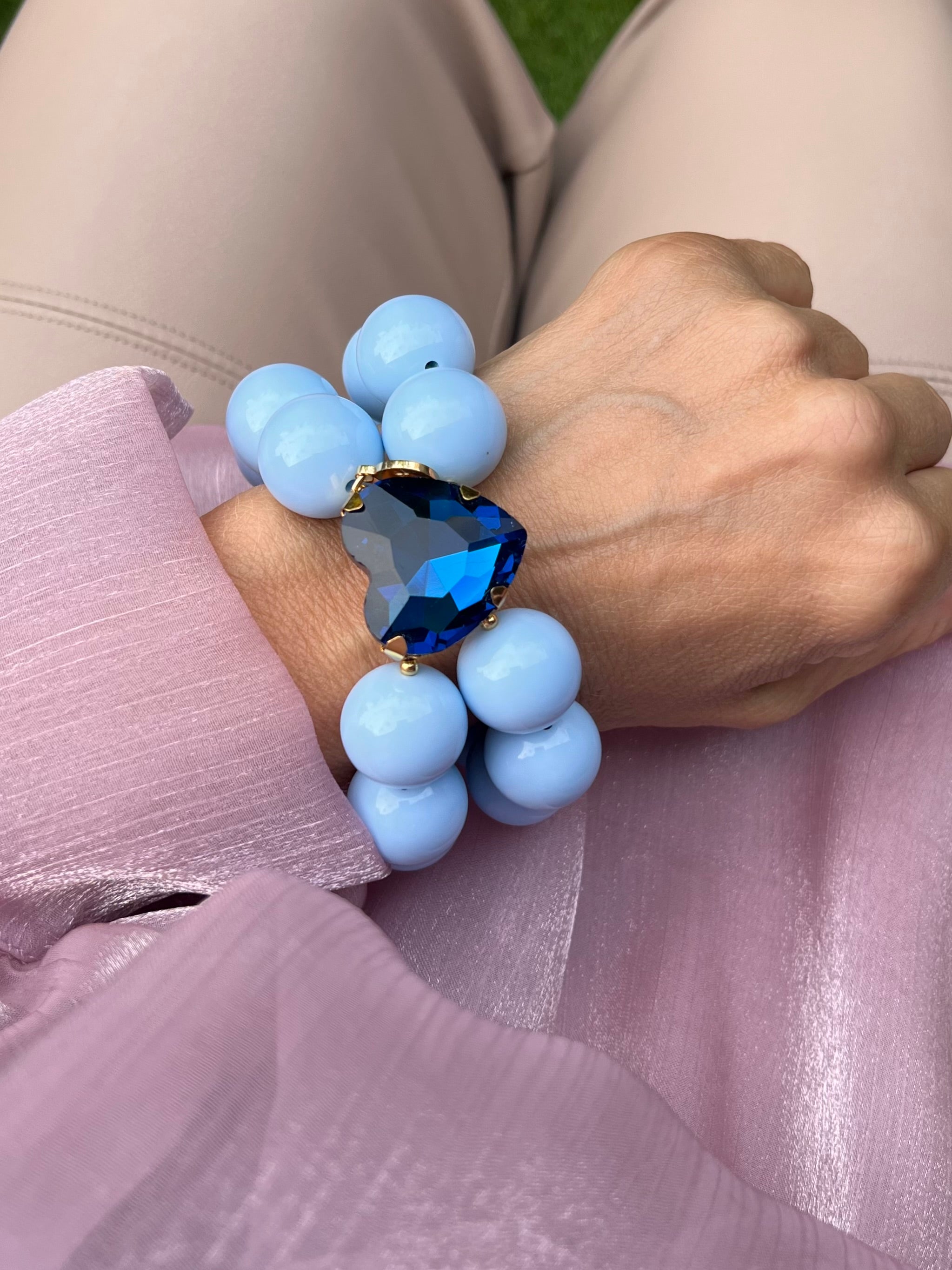 Handgelenk mit blauen Armband aus großen, glänzenden Perlen und einem herzförmigen, tiefblauen Kristall in der Mitte.