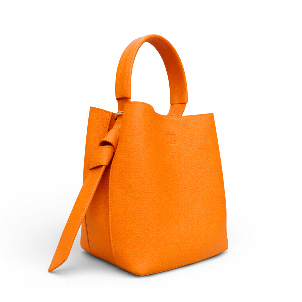 Orange Handtasche aus strukturiertem Leder mit rundem Tragegriff und seitlichem Lederriemen, freigestellt vor weißem Hintergrund.