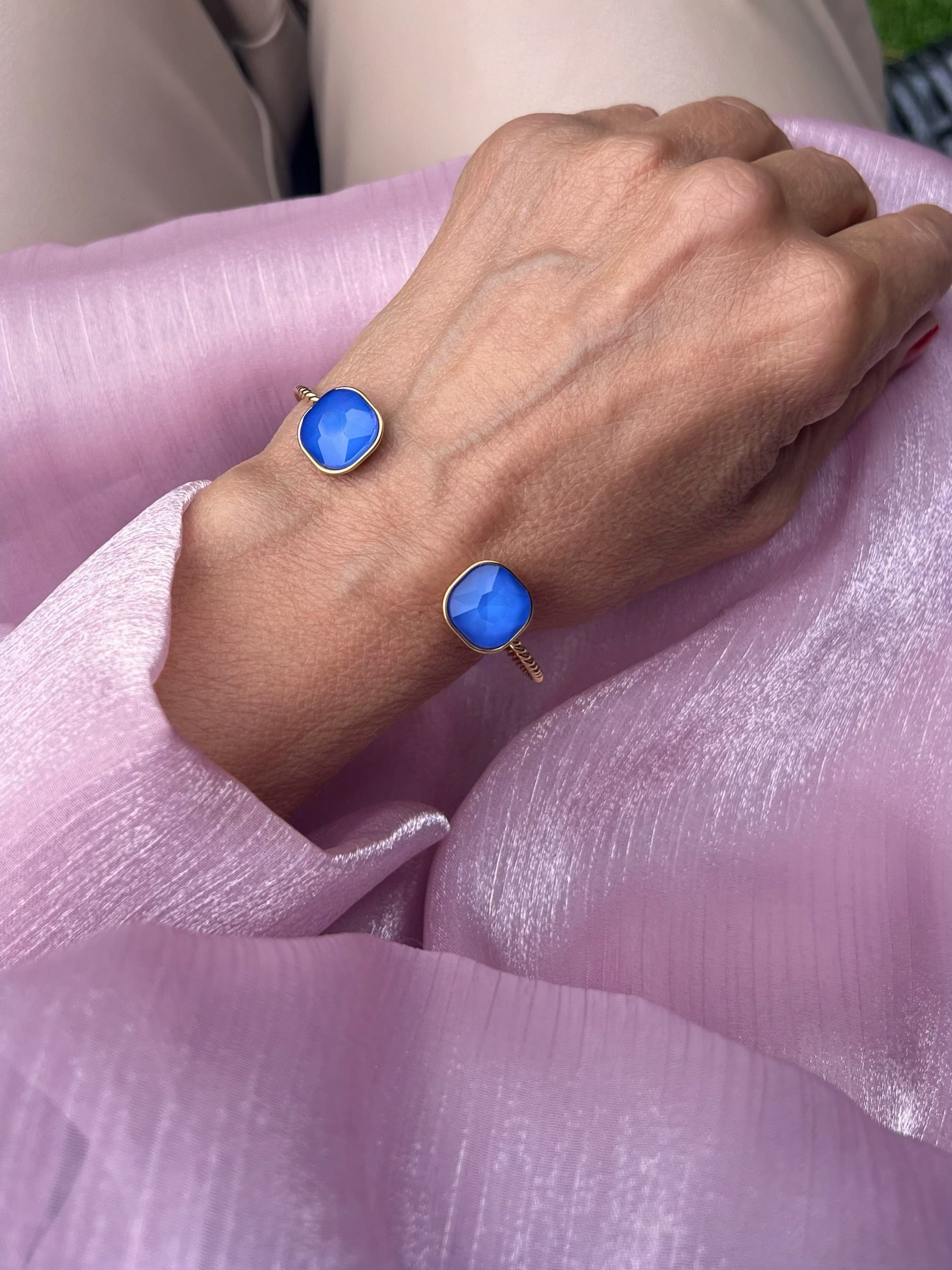 Armreifen in Gold mit blauem Stein, fotografiert an einem Handgelenk.