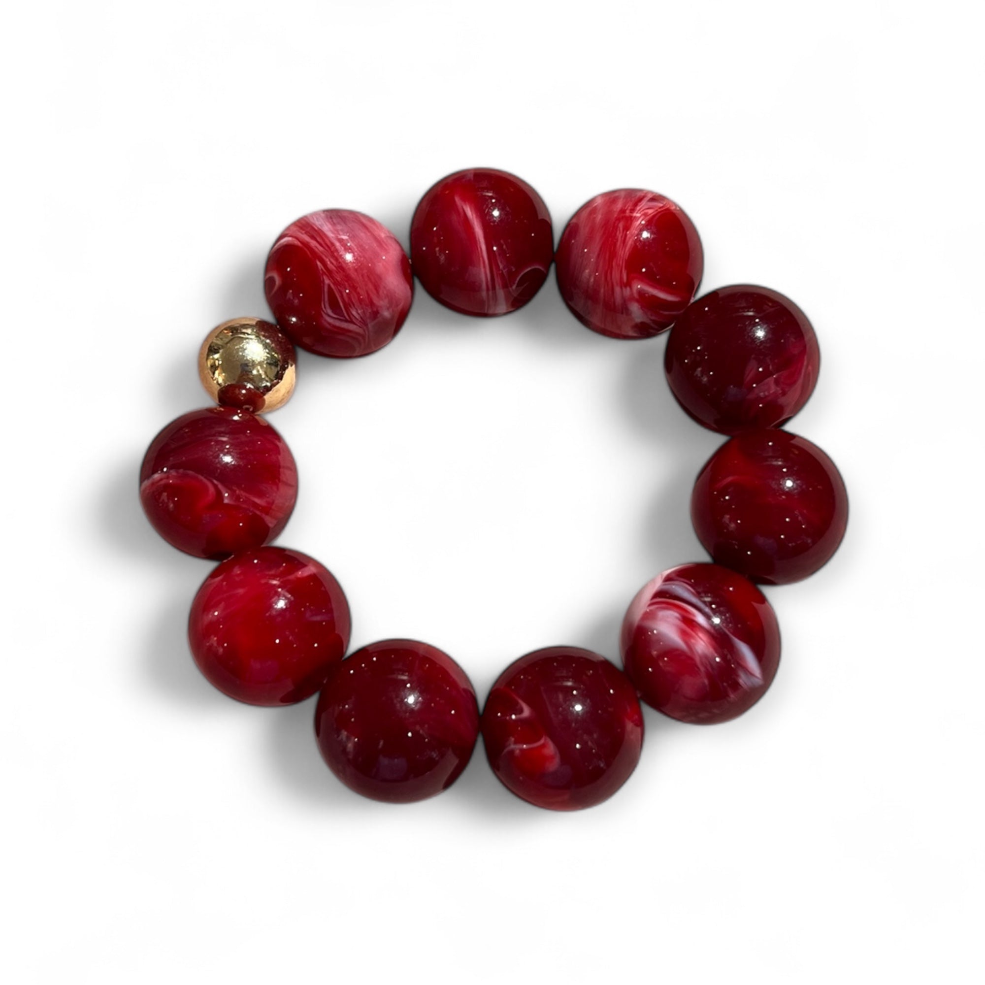 Armband aus roten, marmorierten Kunstharzperlen mit einer goldfarbenen Kugel. Liegt kreisförmig auf weißem Hintergrund.