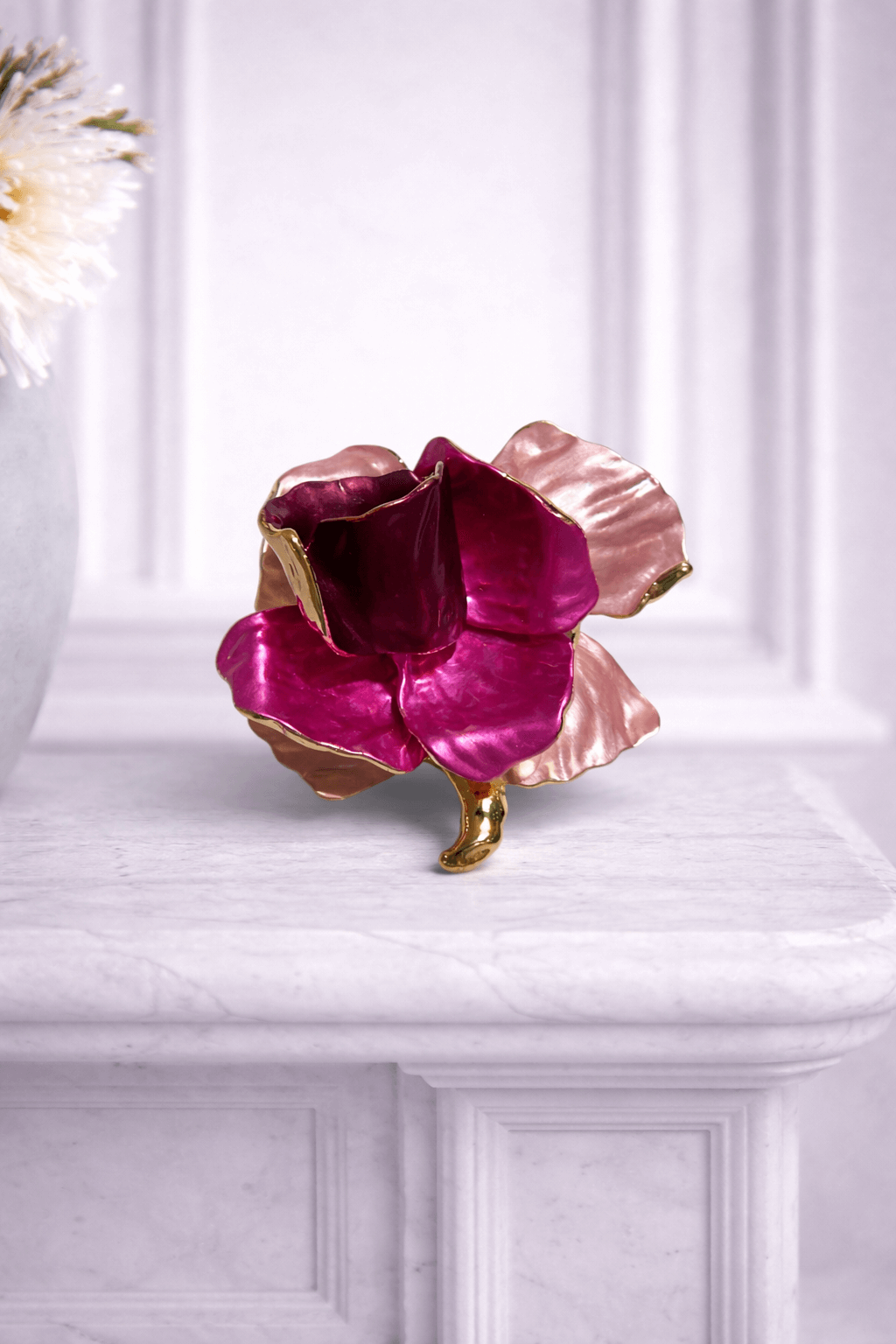 Magnetbrosche in Blütenform mit emaillierten Blütenblättern in Pink und Rosé sowie goldfarbener Einfassung, fotografiert vor hellem Hintergrund.