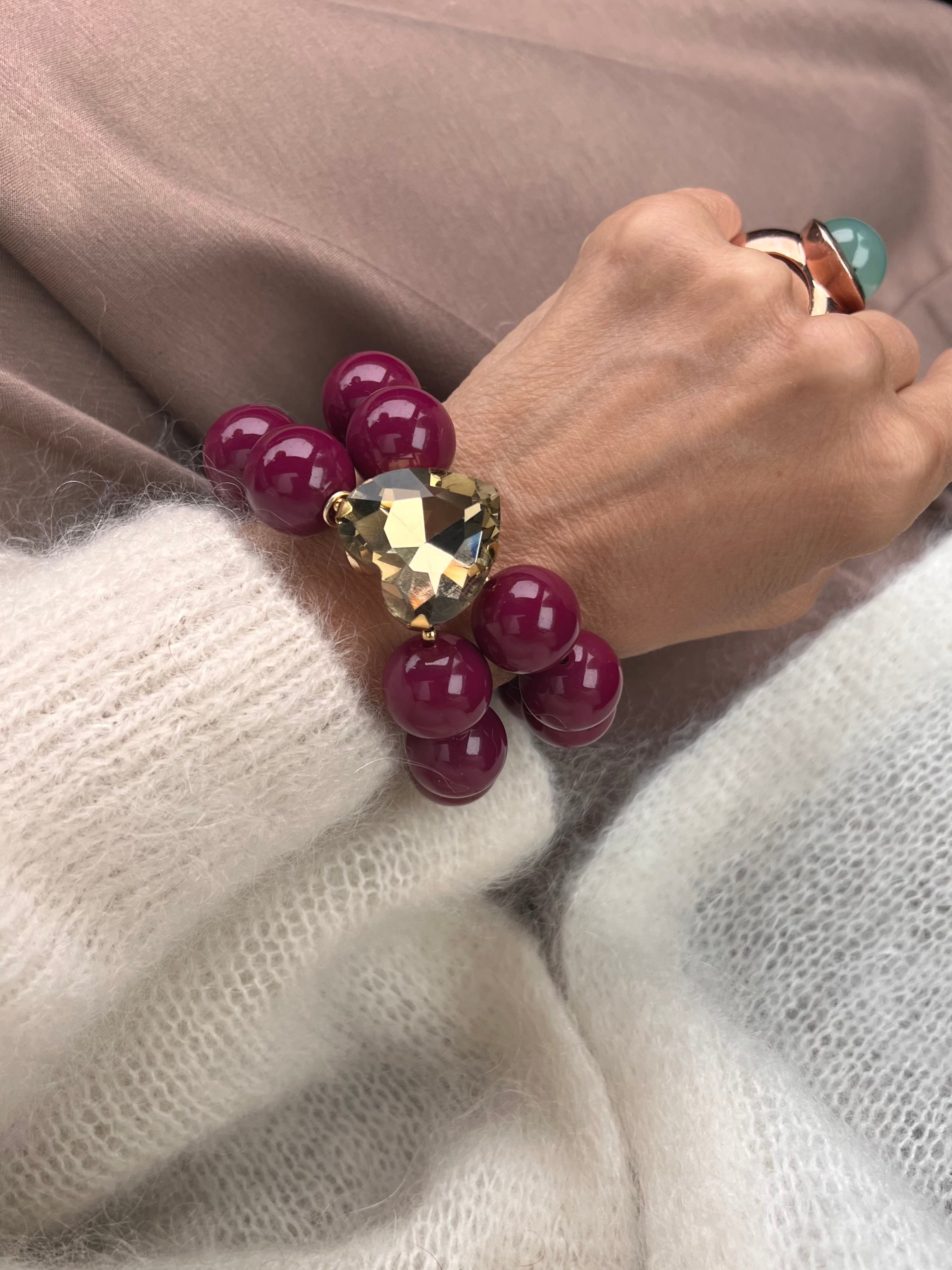 Armband in Burgunder mit großem Herzschmuckstein, und großem Ring. Am Handgelenk auf beigem Stoff fotografiert.