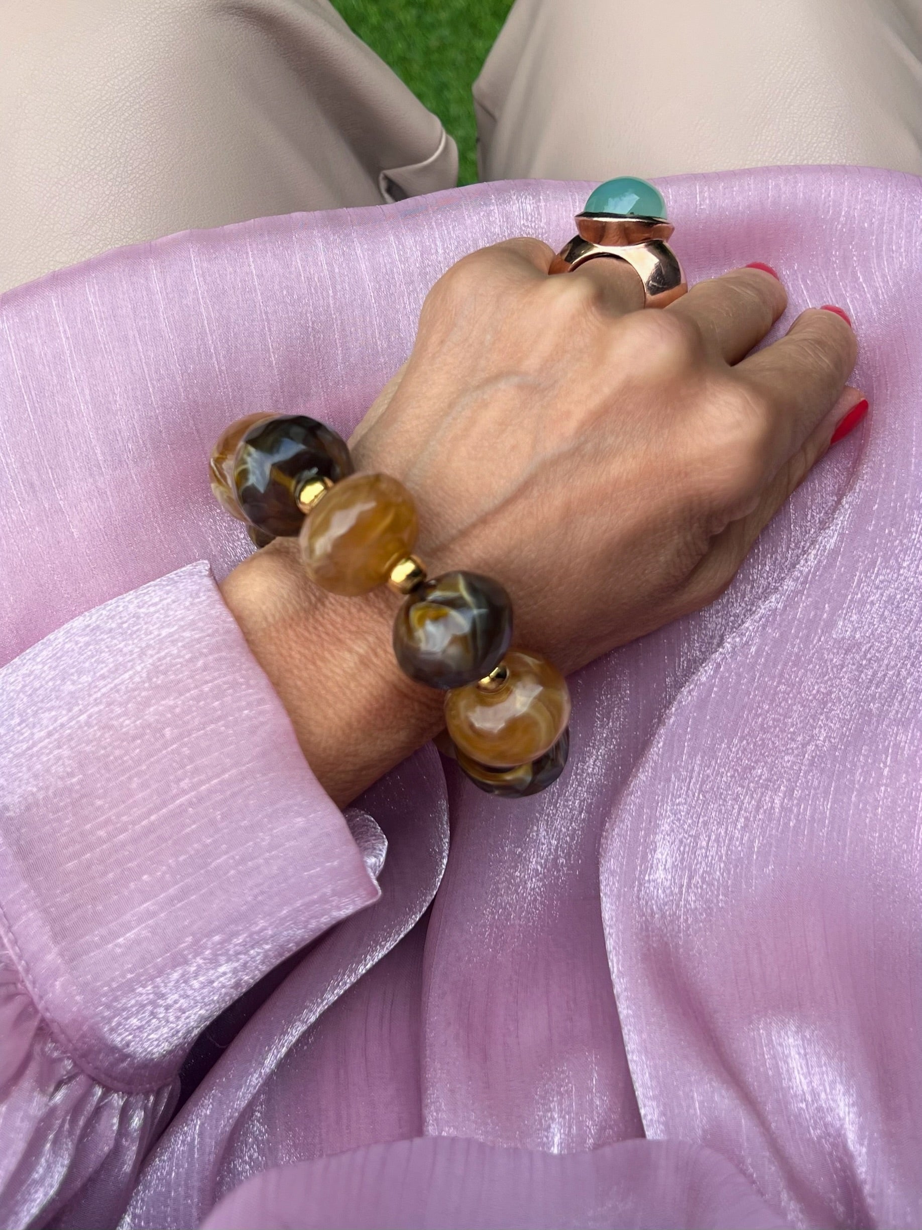 Großes braunes Armband an einem Handgelenk fotografiert auf Rosa Stoff.