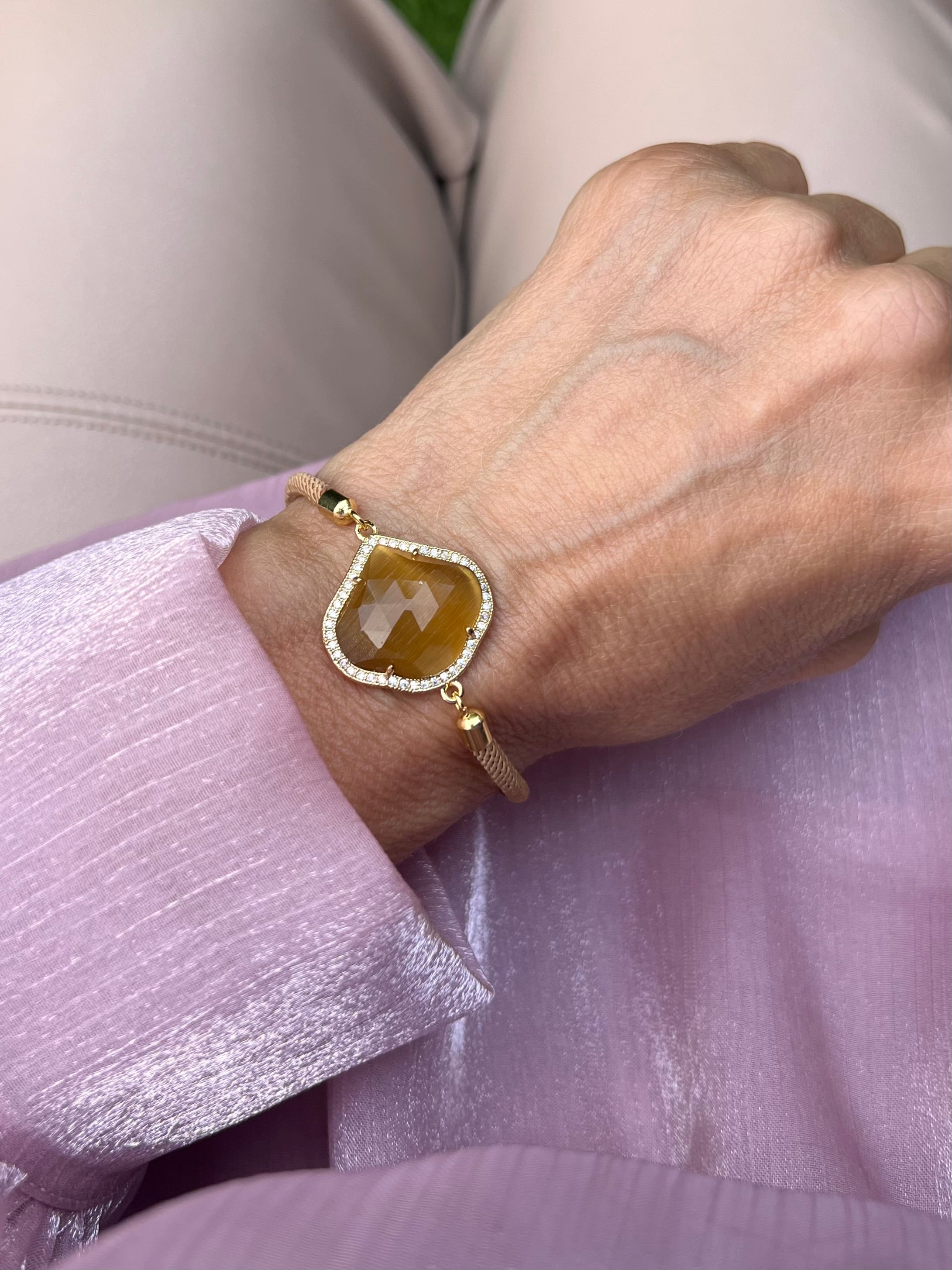 Beiges Armband mit Karamell Schmuckstein an Hand getragen. Auf rosa Stoff fotografiert.