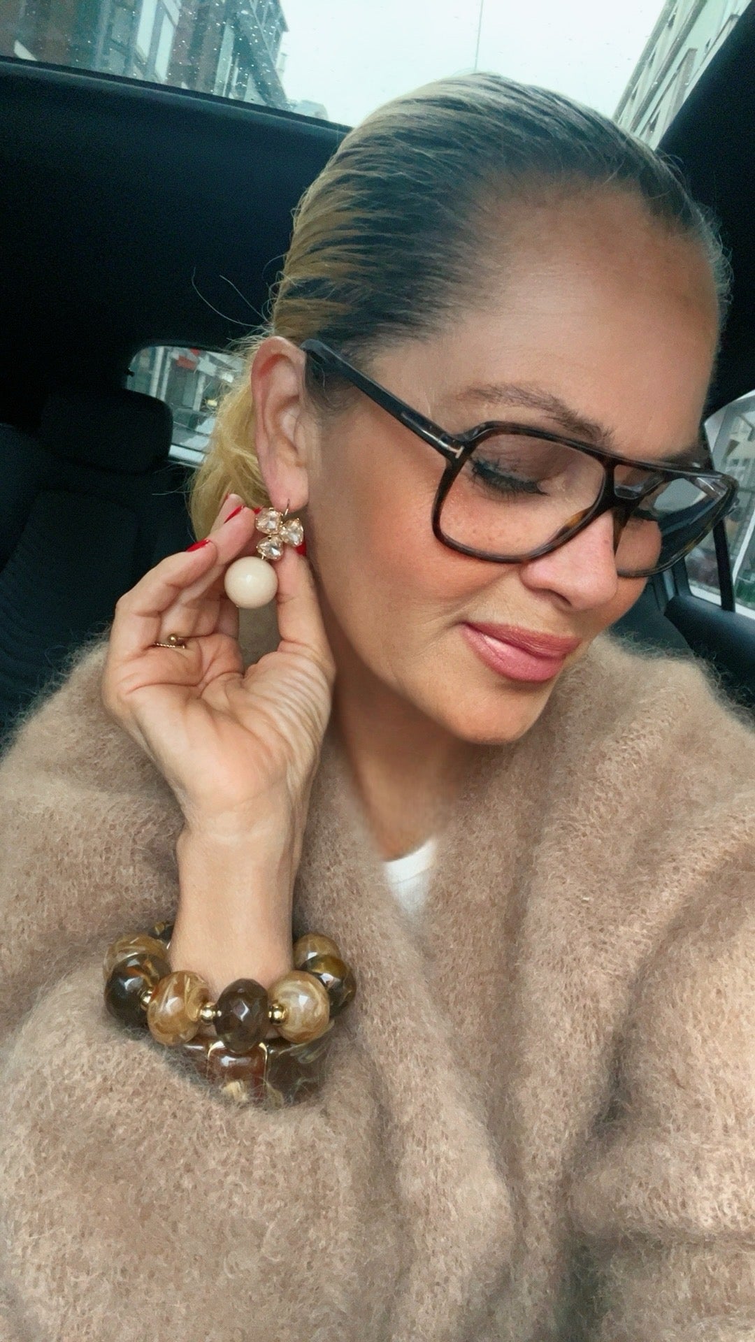 Frau mit eleganten Hänger Ohrringen in goldfarben, kombiniert mit großen Armbändern.