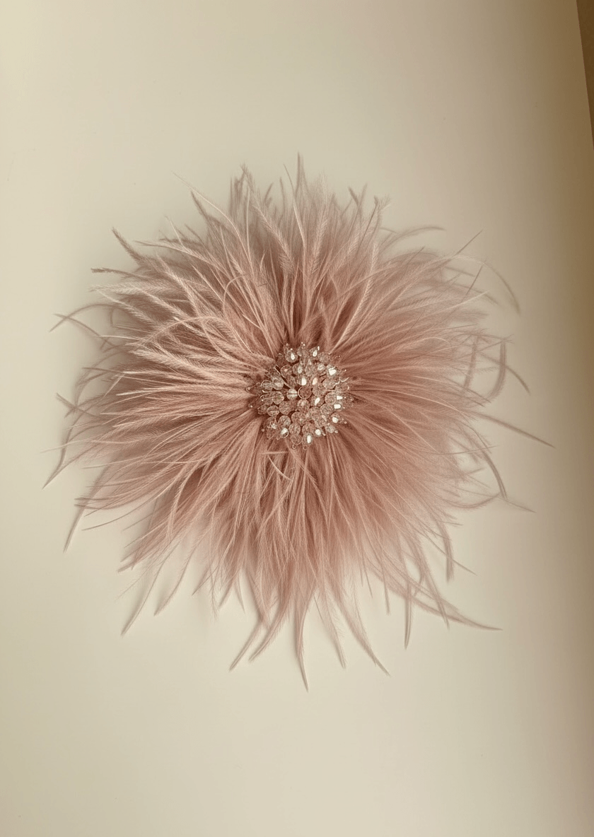 Federbrosche in zartem Rosé mit feinen, leicht voluminösen Federn und mittigem Besatz aus Strass und Perlen, auf hellem Hintergrund.