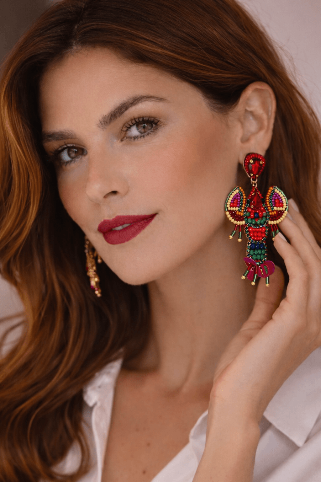 Frau mit schulterlangem rötlichem Haar trägt einen großen, bunten Statement-Ohrring in Hummerform mit Perlen und Steinen; Nahaufnahme von Gesicht und Ohr.