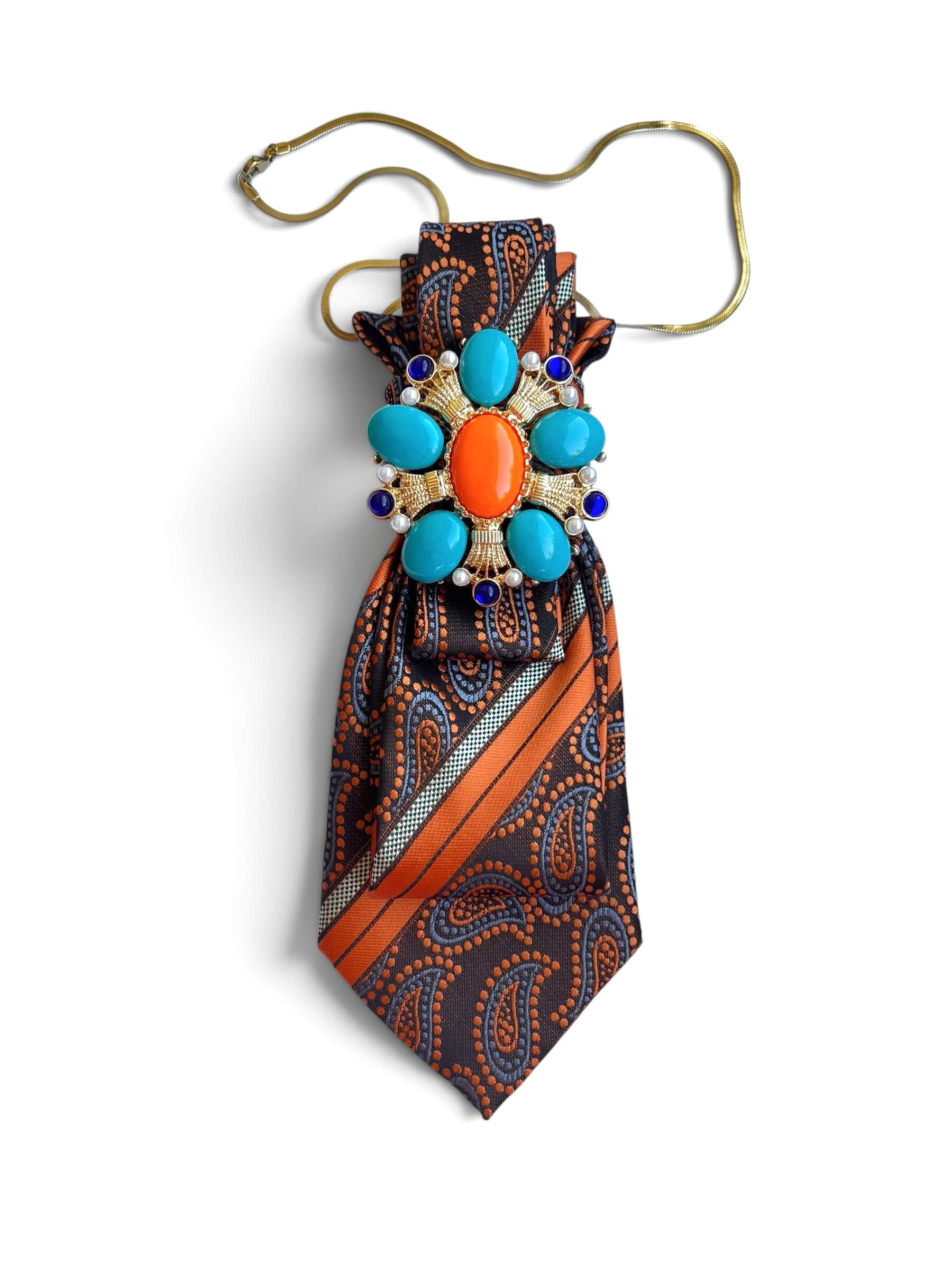 Orangefarbene Krawatte im Paisley Muster mit dekorativer Brosche und goldener Kette auf weißem Hintergrund fotografiert