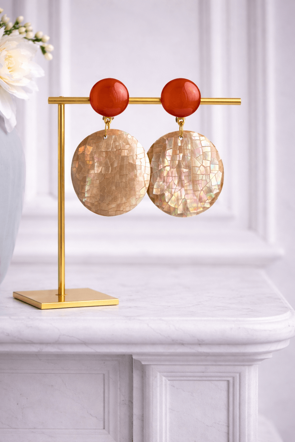 Runde Statement-Ohrringe mit rosé-beigem Stecker und großer Scheibe aus echtem Perlmutt mit schimmernder Mosaikstruktur, präsentiert auf goldfarbenem Schmuckständer.