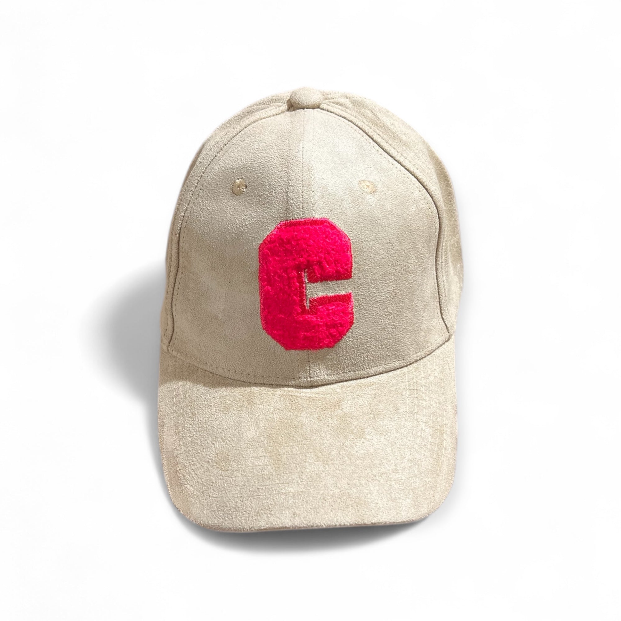 Beige Velours-Cap mit großem pinkem Buchstaben C auf der Vorderseite, fotografiert auf weißem Hintergrund.