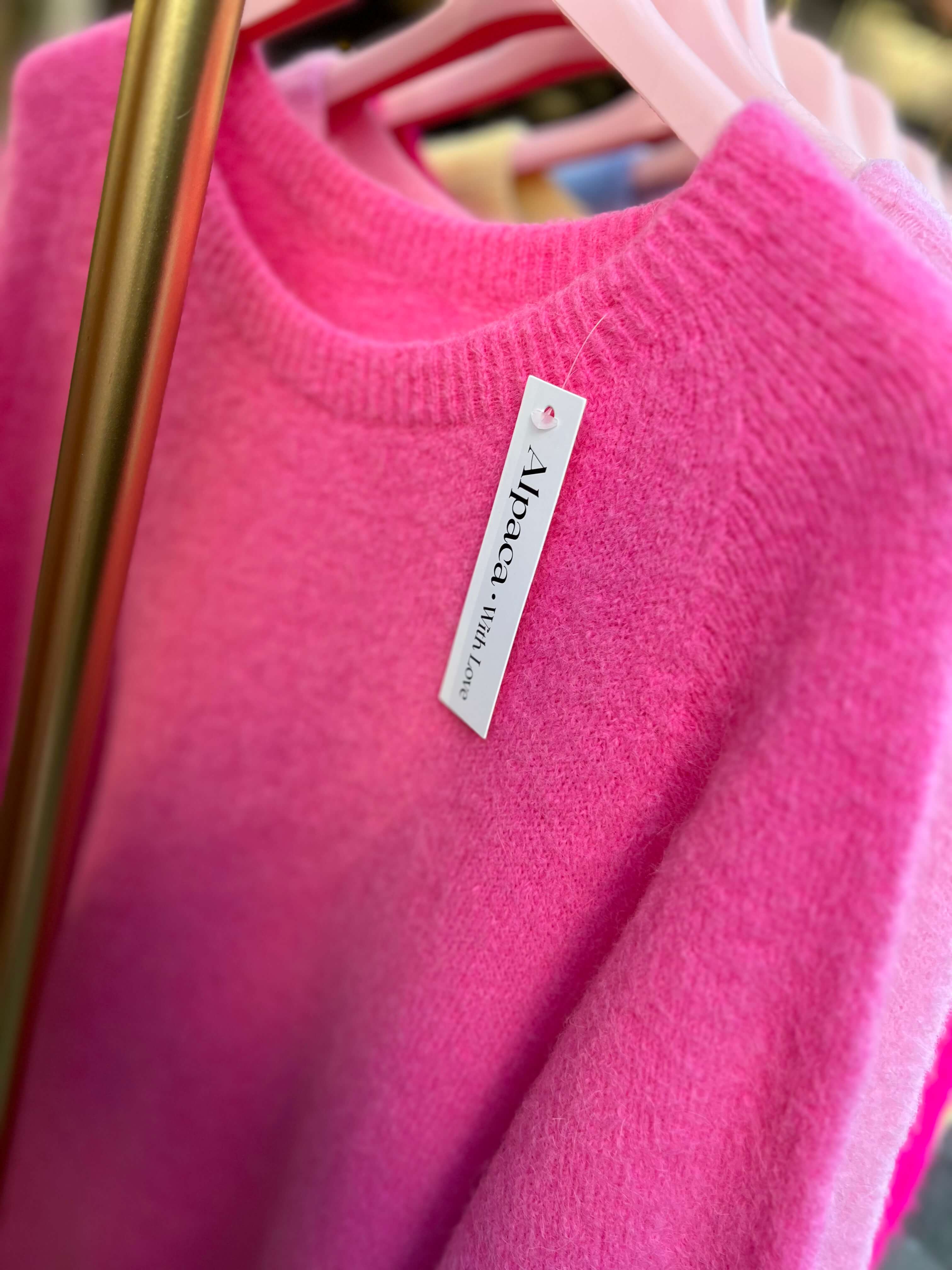 Detailansicht eines pinkfarbenen Baby-Alpaka-Strickpullovers mit sichtbarem Etikett an der Vorderseite.