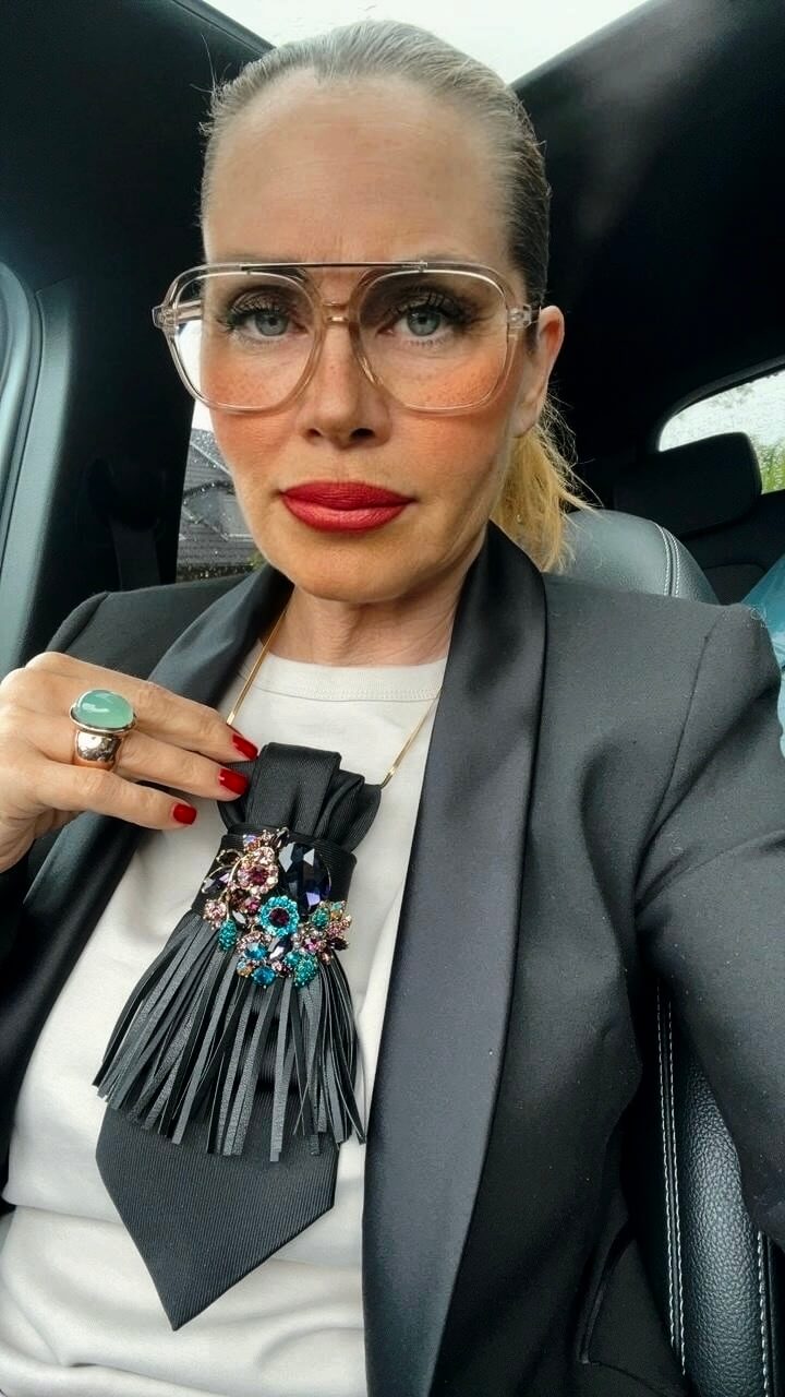 Detailansicht einer schwarzen Vintage-Krawatte mit dekorativer Brosche und Fransen-Detail, getragen mit schwarzem Blazer.