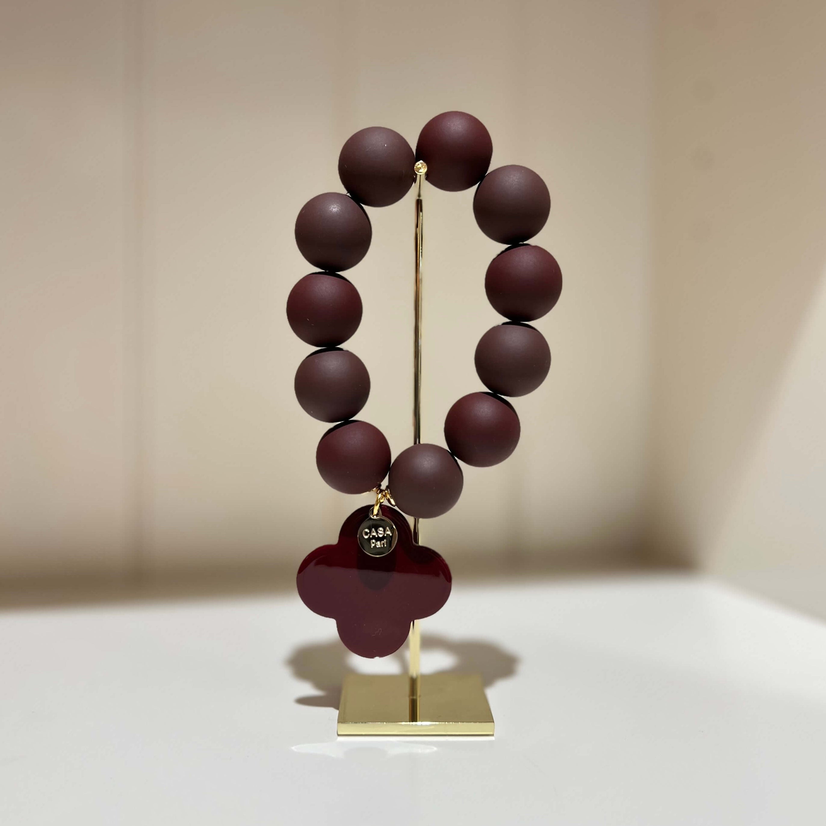 Braunes Armband mit runden Perlen und einem dunklen vierblättrigen Anhänger auf einem Schmuckständer.