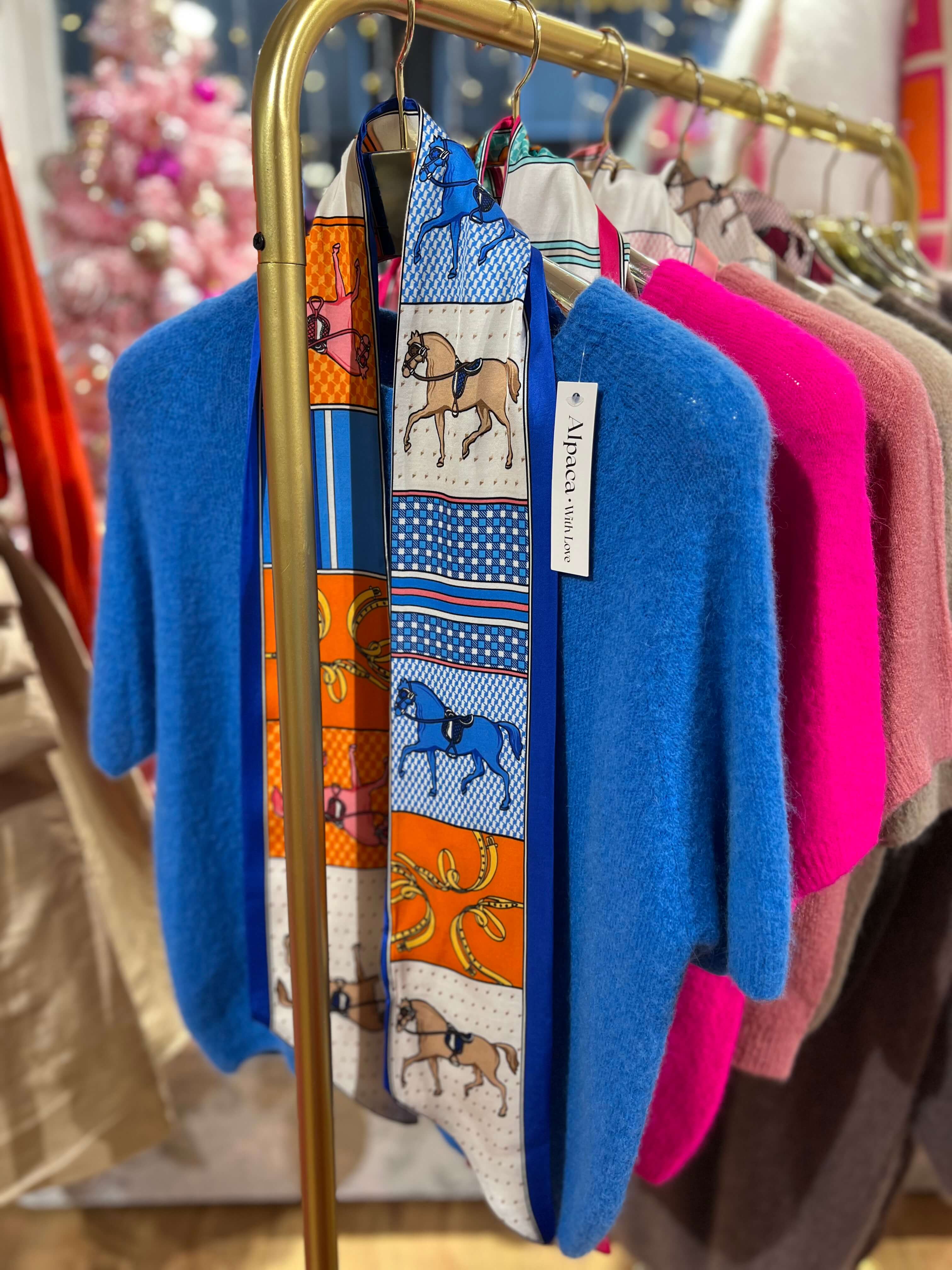 Schmales Seiden-Viskose-Tuch in Blautönen mit grafischem Muster, an einer goldfarbenen Kleiderstange über einem blauen Strickpullover präsentiert.