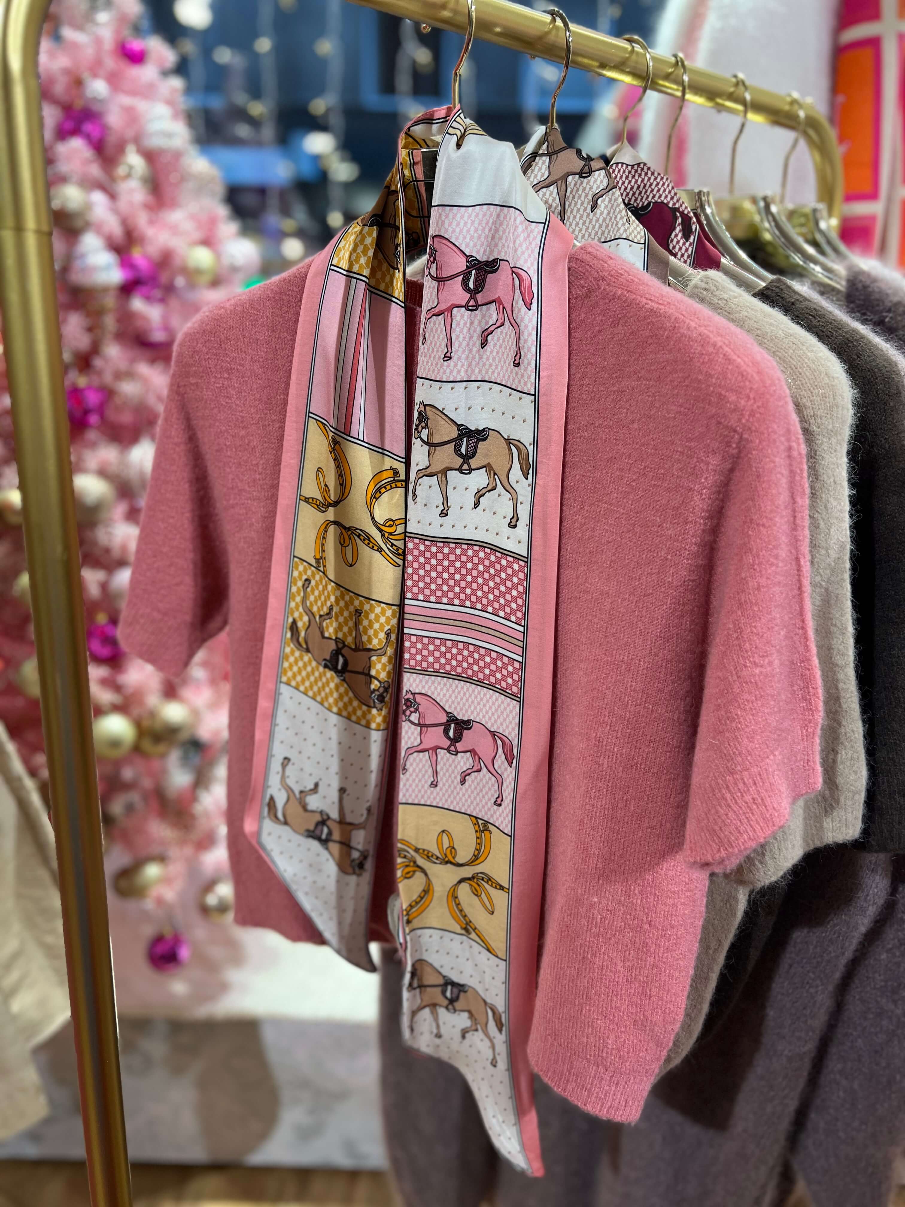 Schmales Seiden-Viskose-Tuch in Rosatönen mit grafischem Muster, an einer goldfarbenen Kleiderstange über einem rosa Strickpullover präsentiert.