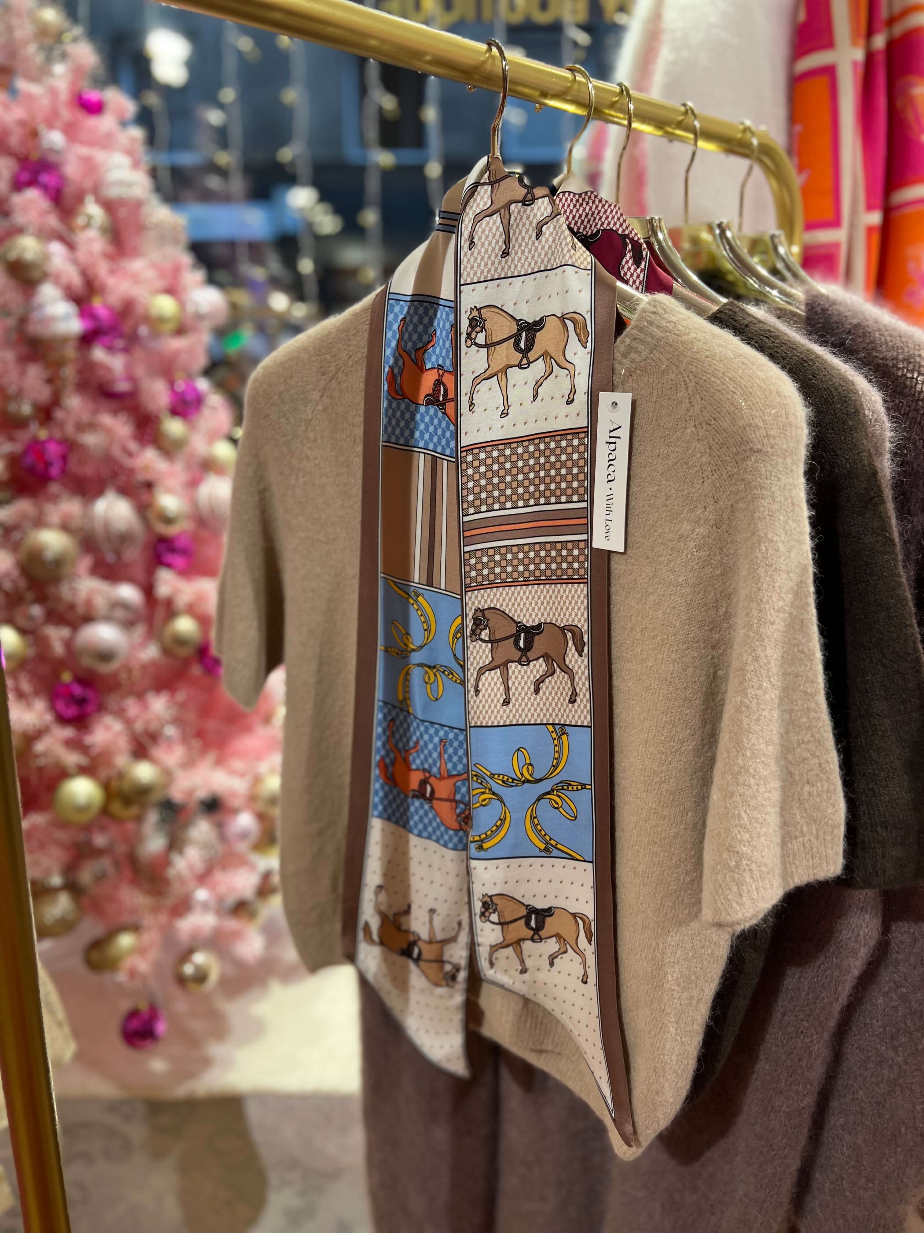 Schmales Seiden-Viskose-Tuch in Beigetönen mit grafischem Muster, an einer goldfarbenen Kleiderstange über einem beigen Strickpullover präsentiert.