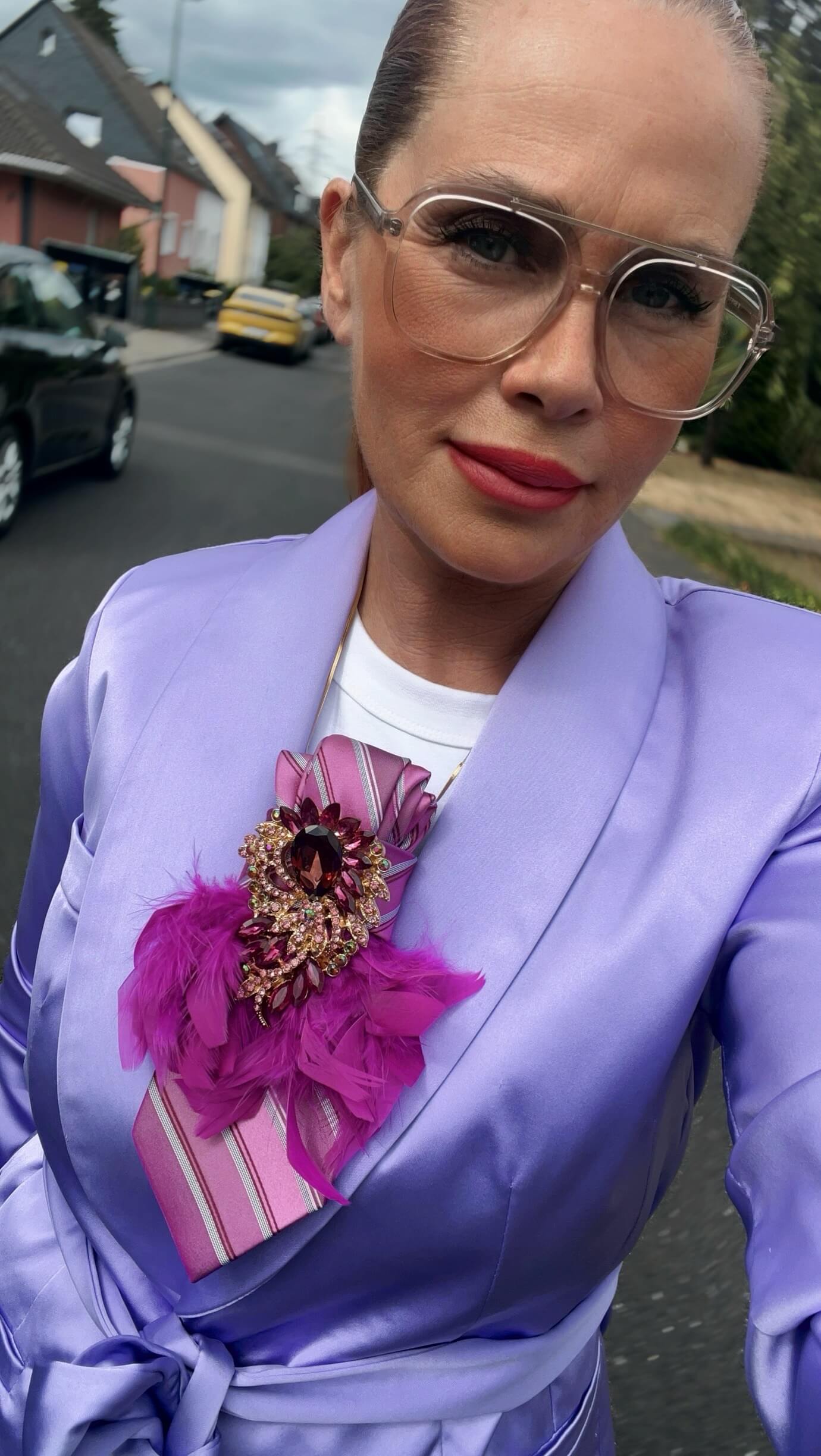 Frau trägt einen Fliederfarben, Bläser mit einer pink lila Brosche mit Federn, Krawatte und steht auf einer Straße