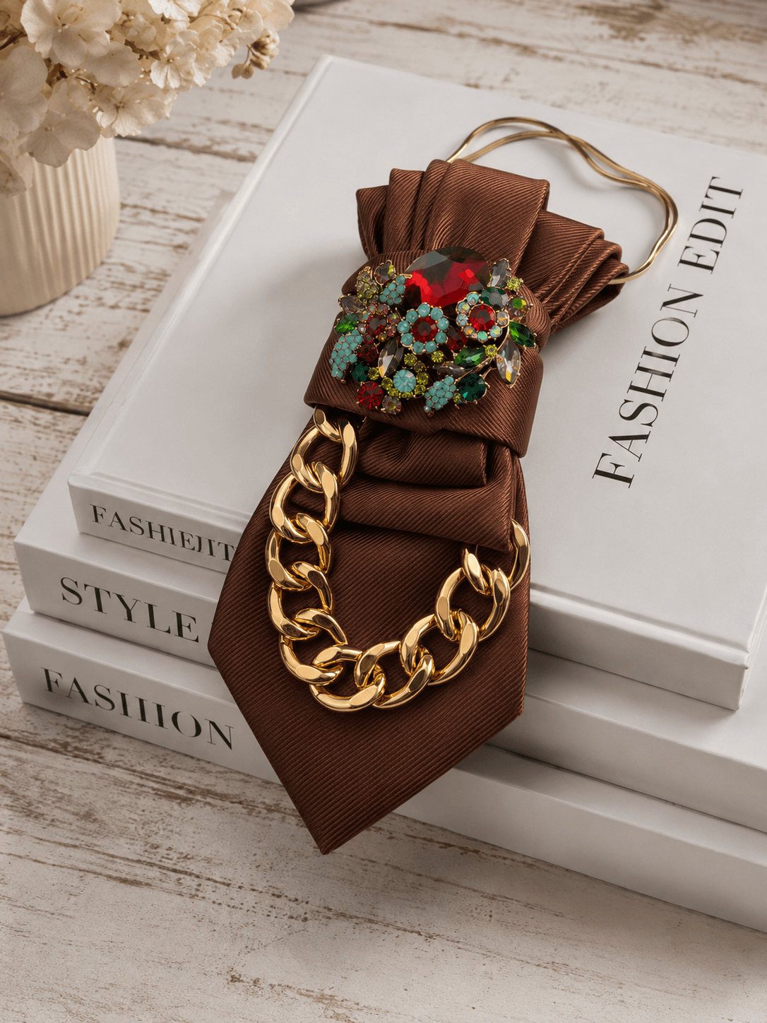 Braune Statement-Krawatte mit goldfarbener Kette und auffälliger Schmuckbrosche. Chocolate Candy verbindet warme Schokoladentöne mit funkelnden Details. Jetzt bei Casapari entdecken.