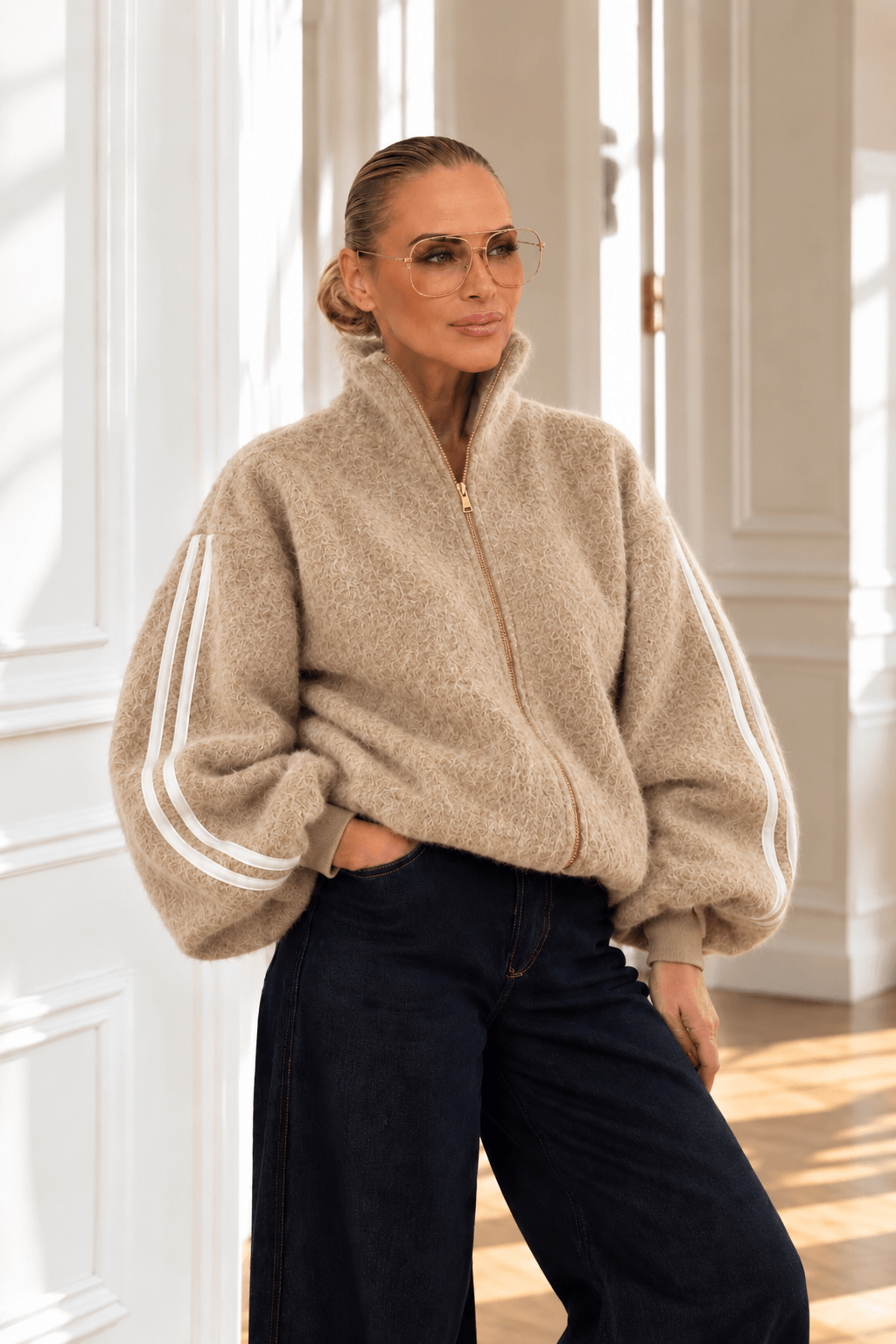 Frau trägt beige Balloon Jacke mit weißen Ärmelstreifen, goldenem Reißverschluss und dunkler weiter Jeans.