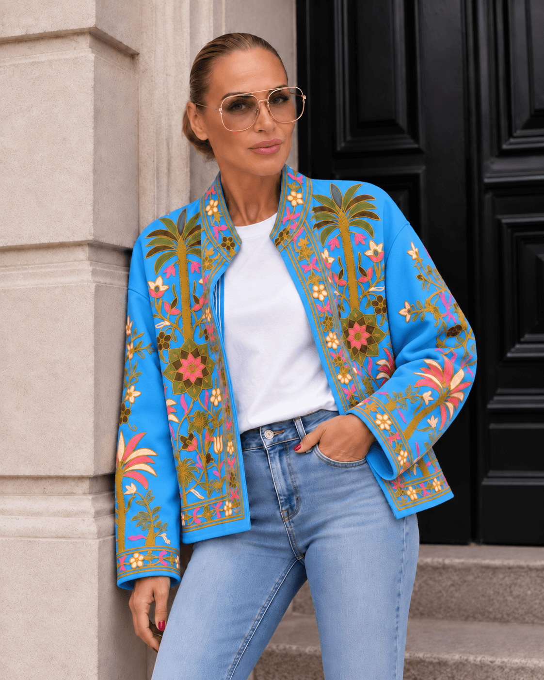 Frau trägt eine leuchtend blaue Oversize-Jacke mit farbenfrohen floralen Stickereien, weißem T-Shirt und heller Jeans.