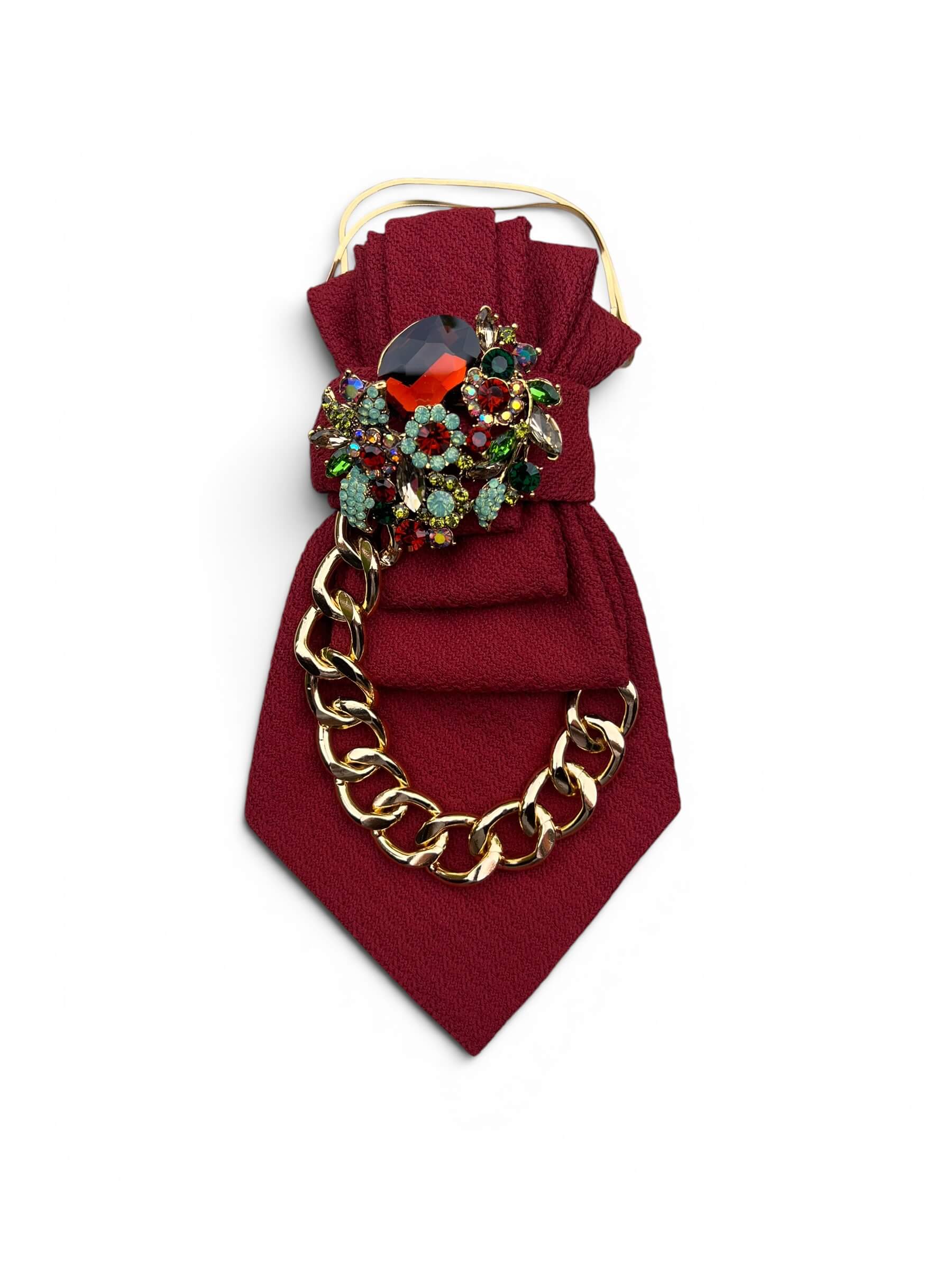 Bordeauxrote Statement-Krawatte mit goldfarbener Kette und funkelnder Schmuckbrosche mit roten, grünen und kristallfarbenen Steinen.