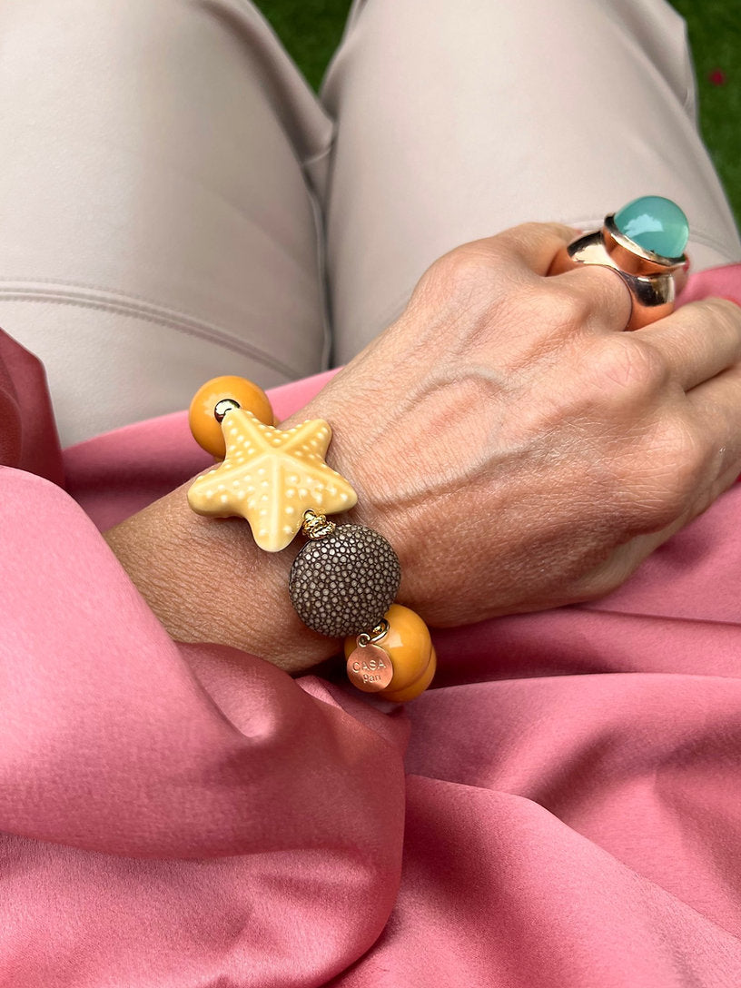 Handgelenk mit gelben Armband aus großen Perlen, verziert mit einem gelben Seestern und einem runder Perle.