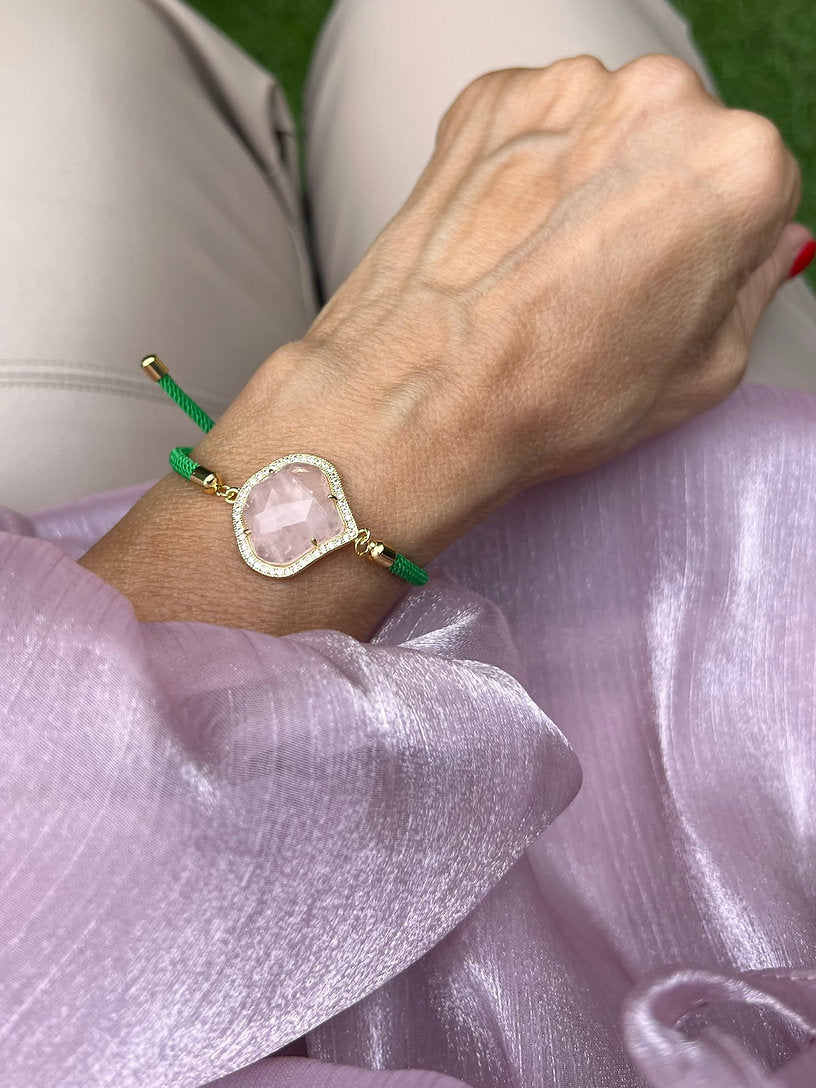 Grünes Armband mit Rose Schmuckstein an Hand getragen. Auf rosa Stoff fotografiert.