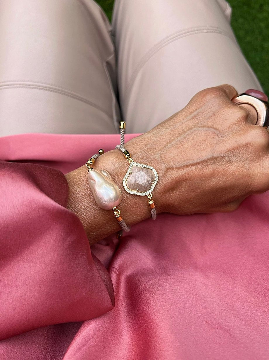 Nahaufnahme einer Hand mit zwei Armbändern. Rosa mit großer Barockperle und goldfarbenen Details.