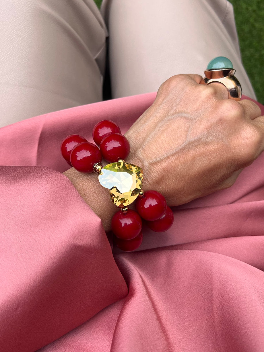 Handgelenk mit auffälligem Armband aus großen roten Perlen und einem großen topasfarbenen Kristall, kombiniert mit einem Statement Ring mit türkisfarbenen Stein.