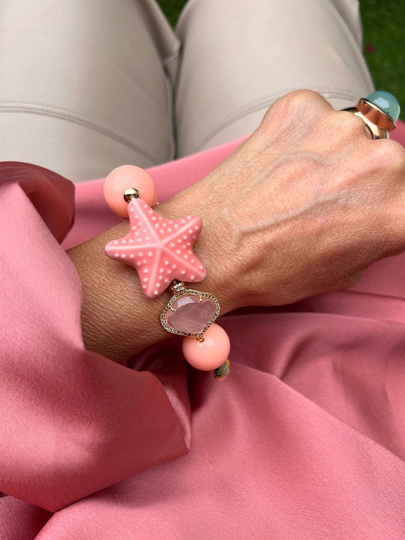 Handgelenk mit rosa Armband aus großen Perlen, verziert mit einem piken Seestern und einem herzförmigen Kristall.