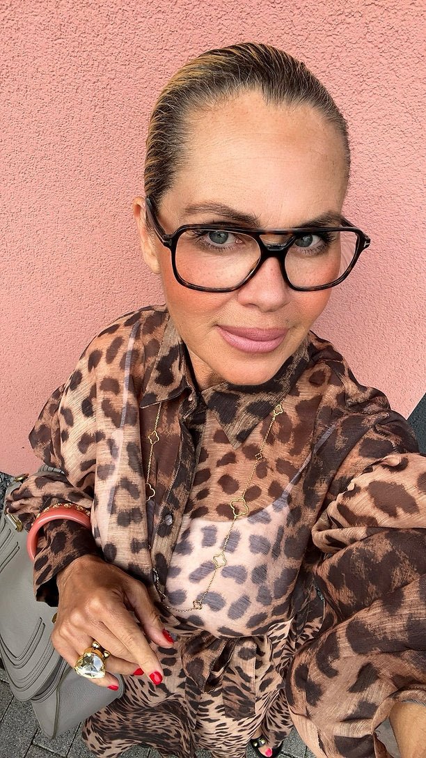 Frau trägt fließendes Kleid im Leopardenmuster mit Bindegürtel, kombiniert mit auffälliger Brille.