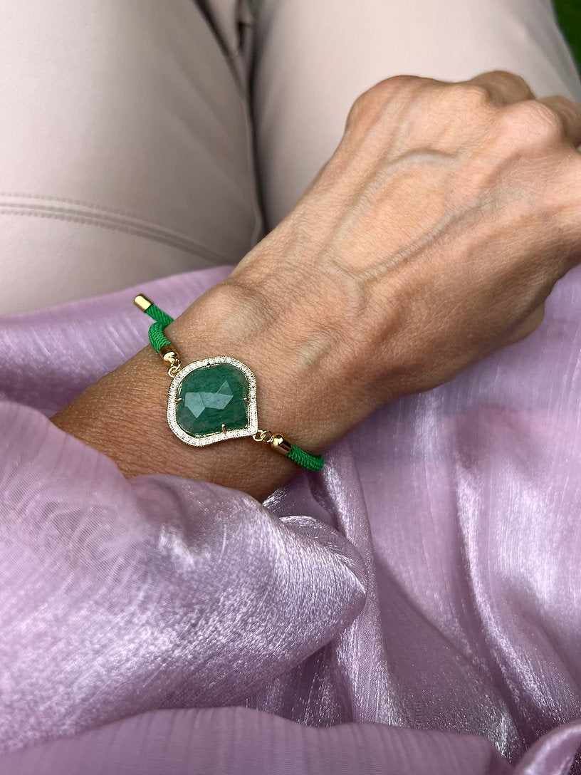 Grünes Armband mit grünem Schmuckstein an Hand getragen. Auf rosa Stoff fotografiert.