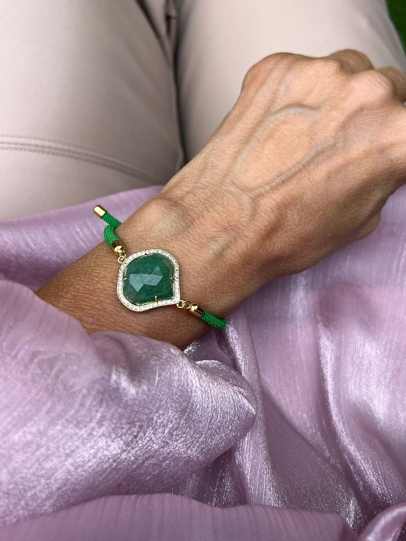 Grünes Armband mit grünem Schmuckstein an Hand getragen. Auf rosa Stoff fotografiert.