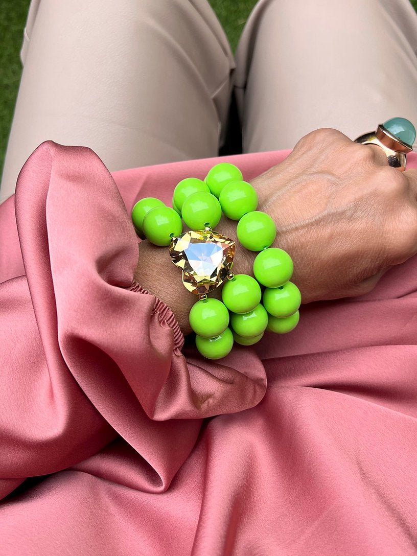 Grüne Armbänder aus Perlen mit Kristall Herz in der Mitte. An Hand auf rosa Stoff.