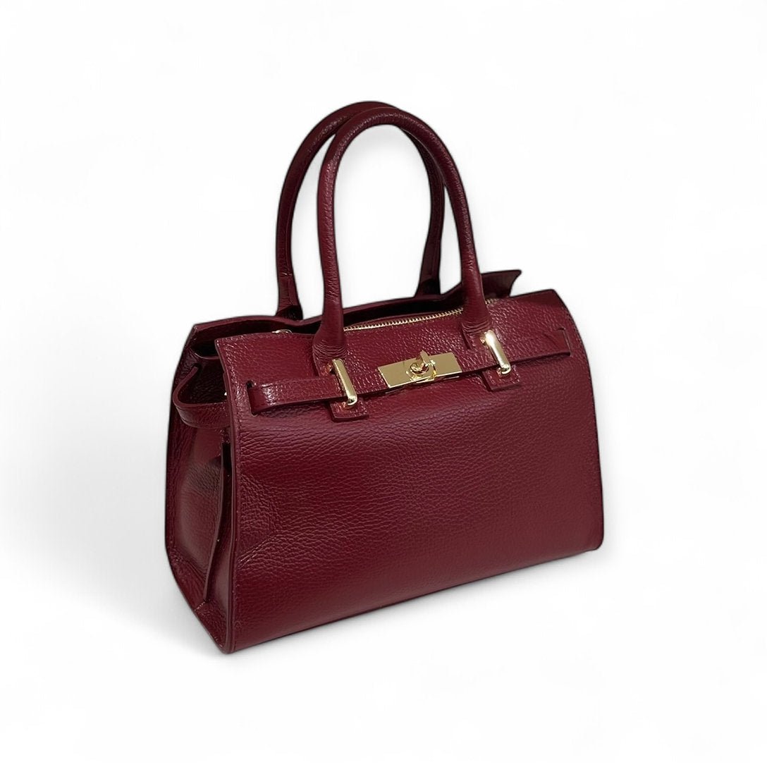 Burgundy Ledertasche mit goldfarbenem Verschluss, zwei Henkeln und abnehmbarem Schultergürtel, auf hellem Hintergrund fotografiert.