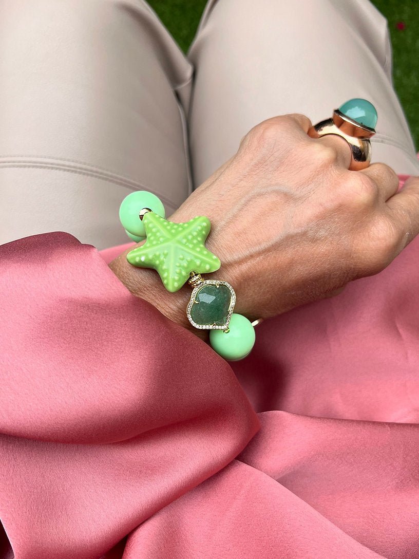 Handgelenk mit Armband aus großen Perlen, in Mintfarben verziert mit einem grünen Seestern und einem herzförmigen Kristall.